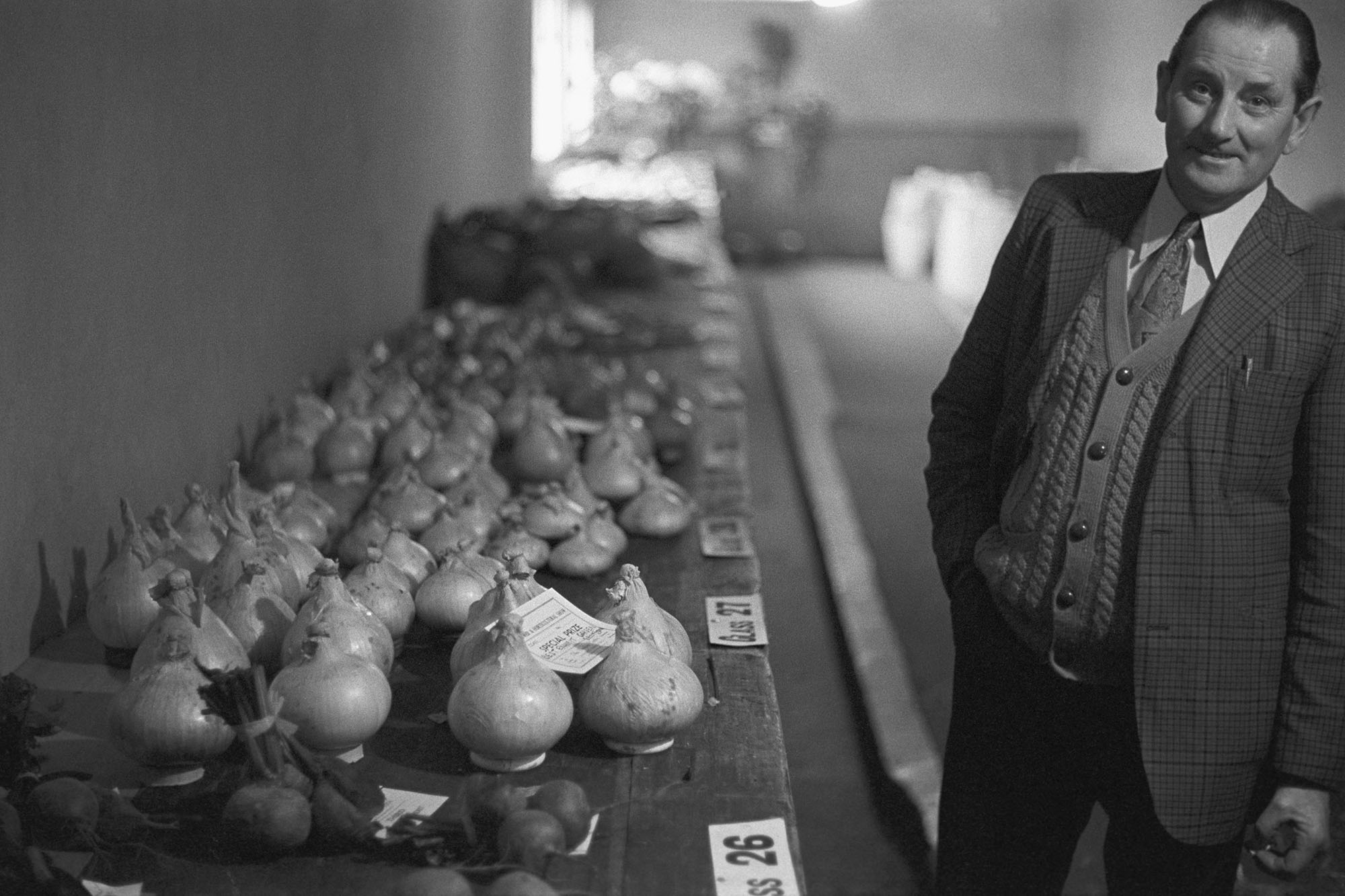 Man standing beside his prize winning onions.
[Bill Smale standing by a table with a display of onions at St Giles in the Wood Flower Show.]