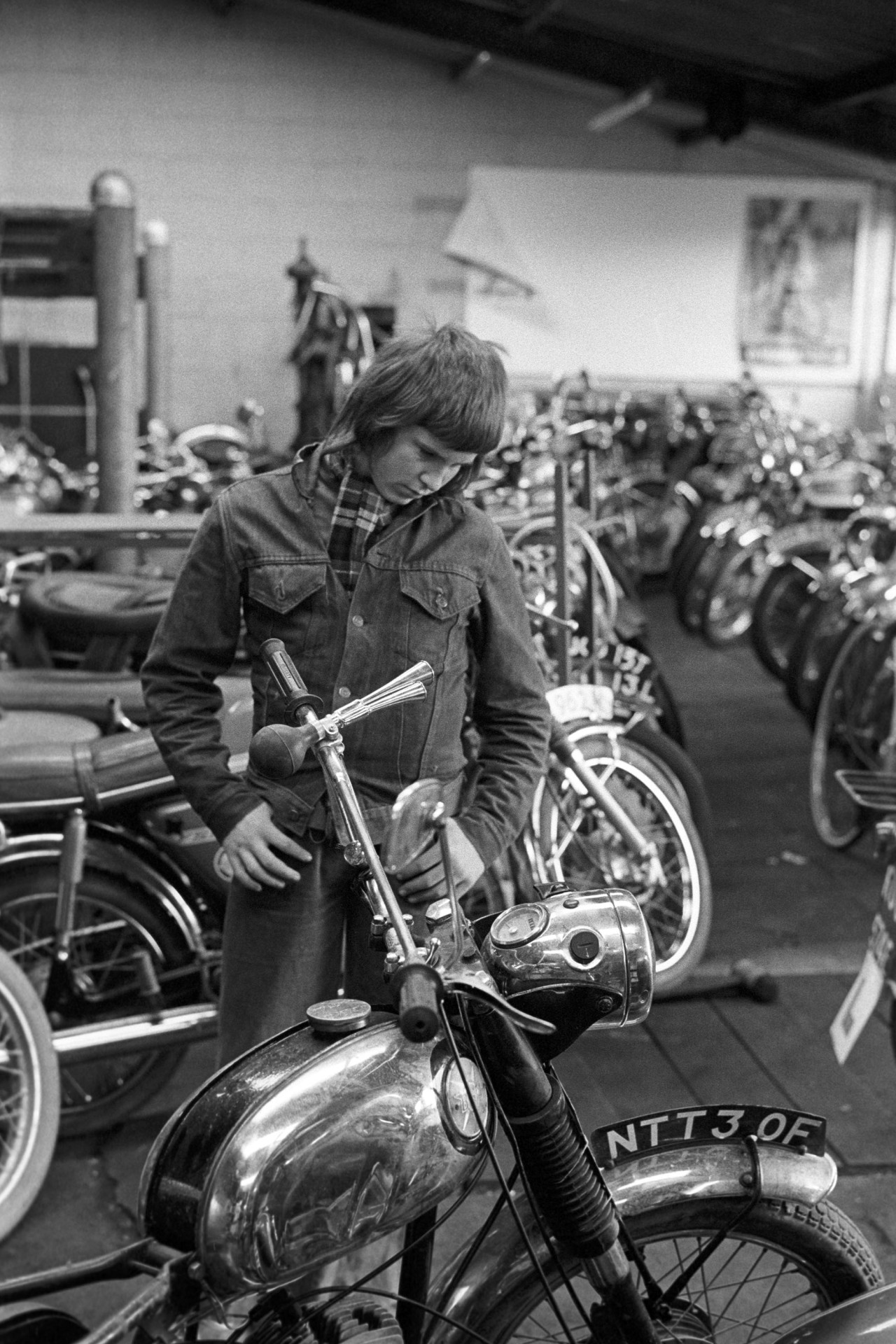 Young man looking at motor bikes in showroom.
[A young man in a denim jacket, looking at a BSA motorbike in Les Smale's showroom in Calf Street in Torrington.]