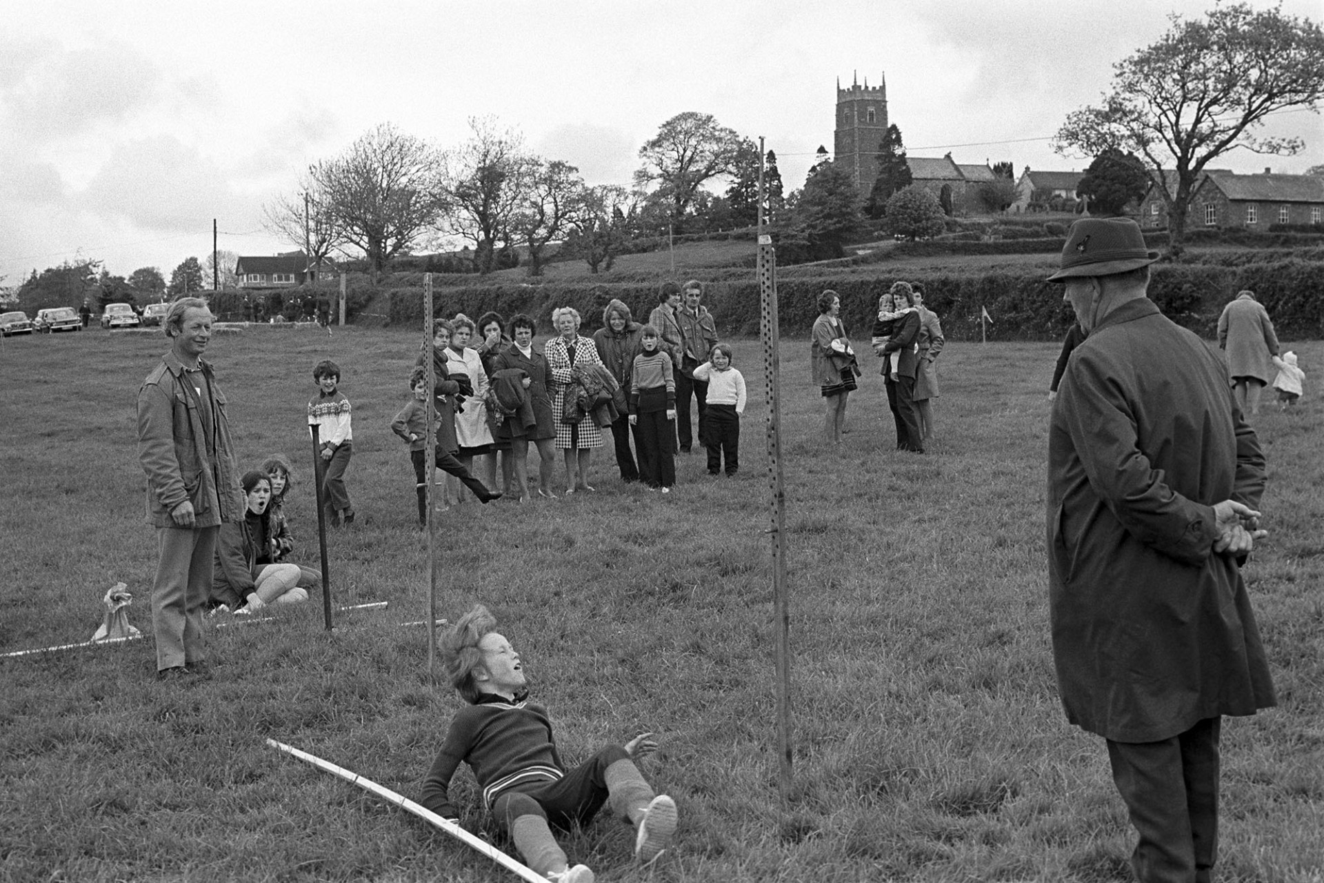 Sports at Club Day, High jump.
[Children taking part in the high jump at Iddesleigh Club Day with a group of people watching. Iddesleigh church tower is visible in the background.]