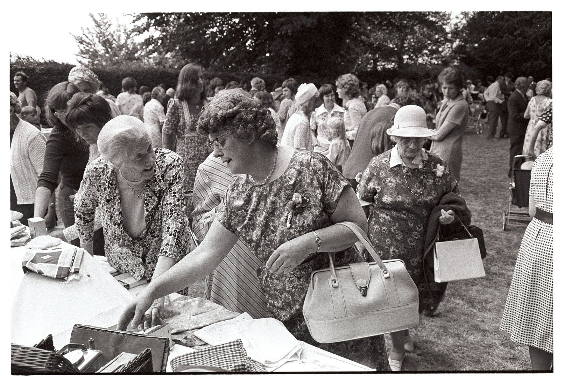 Church Garden Party, women at jumble stall.
[A woman examining items on a jumble stall at the Chulmleigh Church Garden Party in the grounds of Chulmleigh Vicarage.]