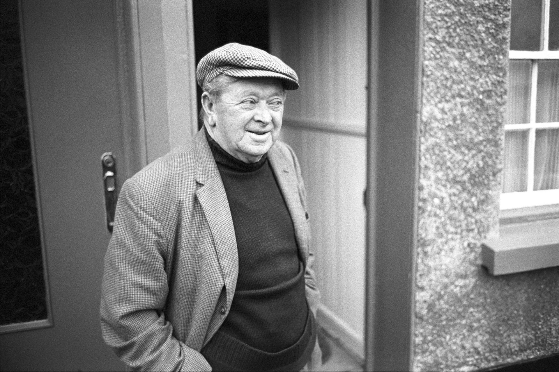 Man in cap standing outside house.
[Billo Griffiths, wearing a flat cap, standing outside a house in Appledore.]