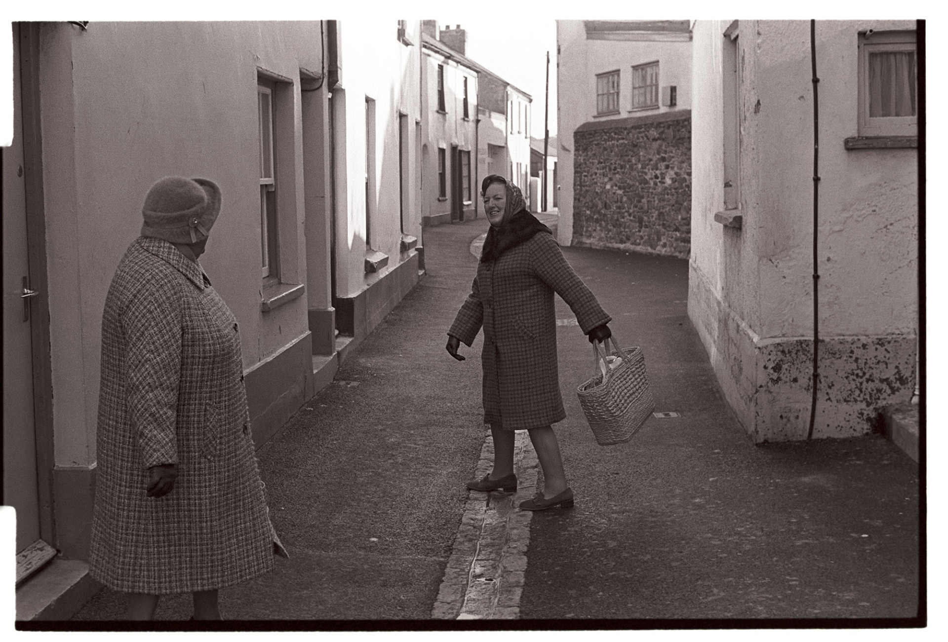 Street scene, two women chatting.
[Two women, one with a shopping bag, chatting in a narrow street in Appledore.]