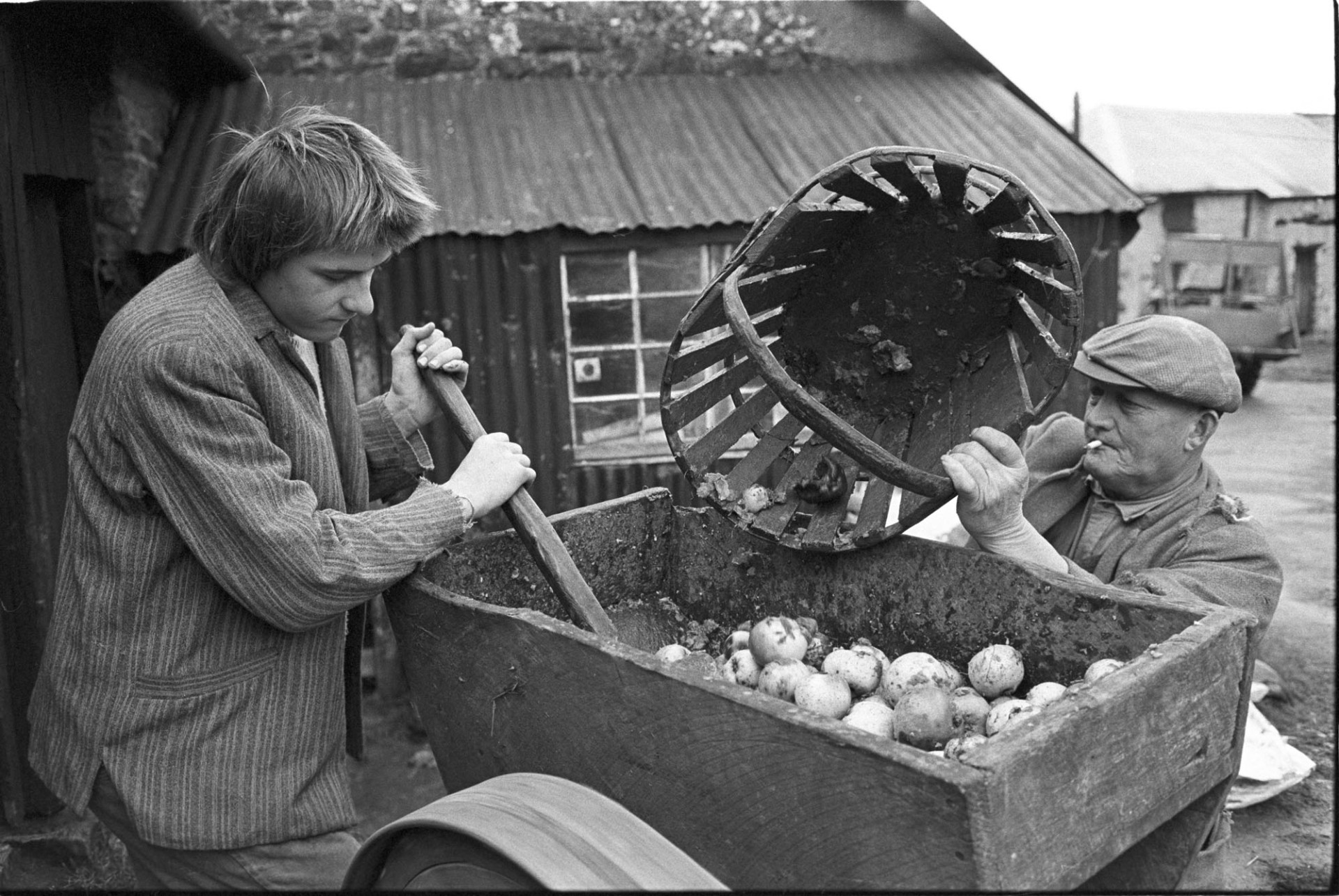 Men using apple crusher.<br />
[Mr Eastman and another man using an apple crusher at Hacknell, Burrington.  One man is loading it with a trug of apples, the other is pushing the apples through the crusher.]