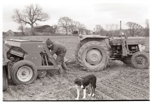 Farmer checking a seed drill by James Ravilious