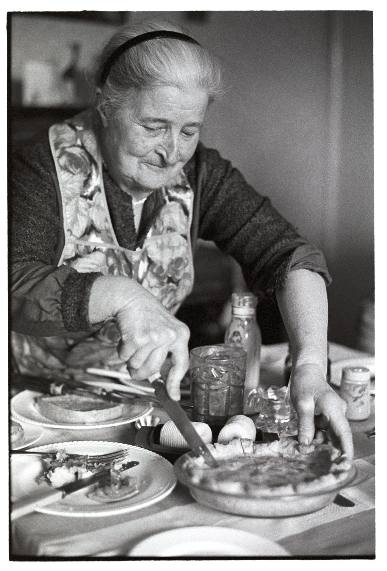 Woman cutting slice of home made pie.
[Norah Maynard cutting a slice of home made pie at her kitchen table in Atherington.