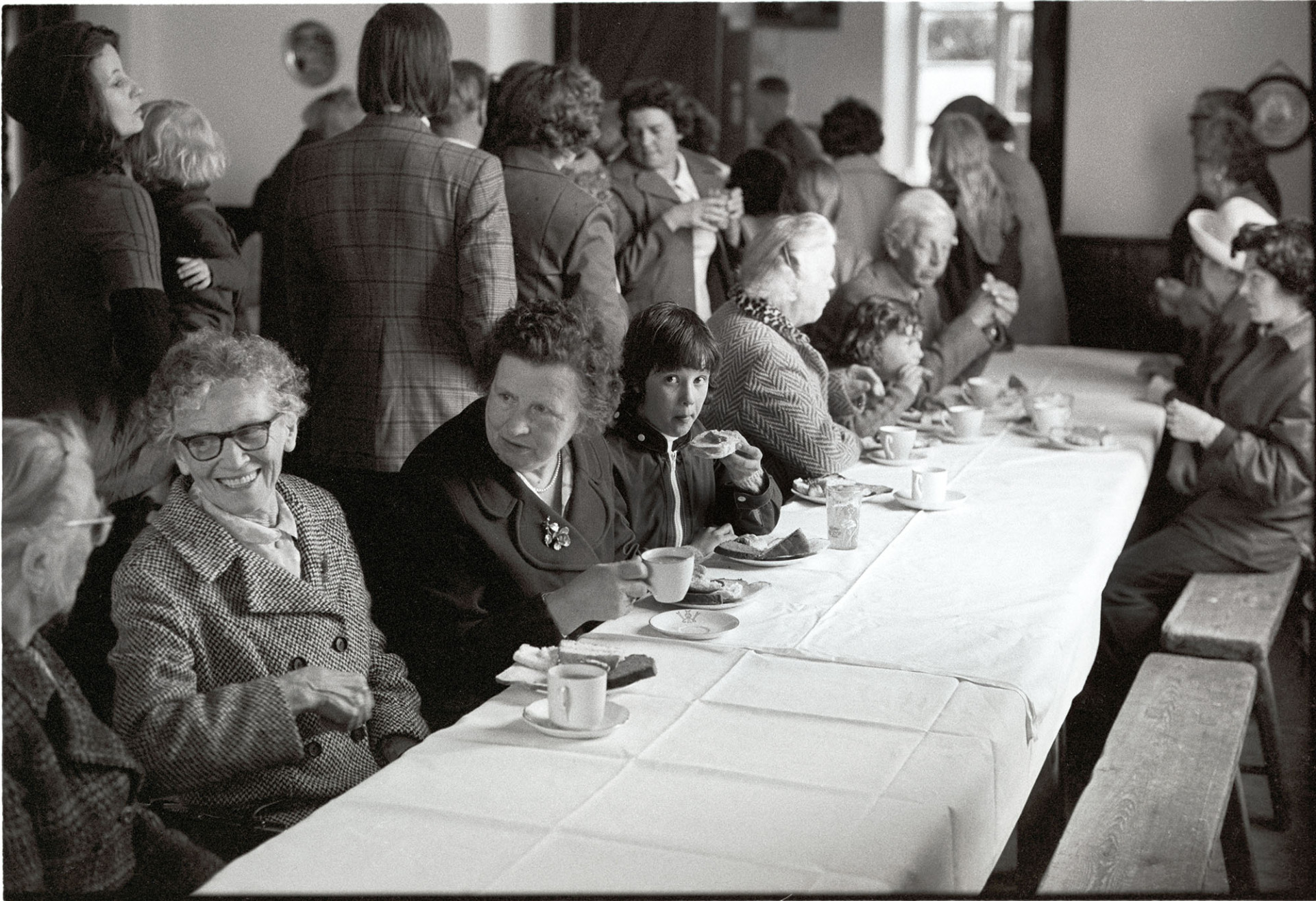 People having tea in village hall.
[People having tea and chatting in the village hall at Iddesleigh.]