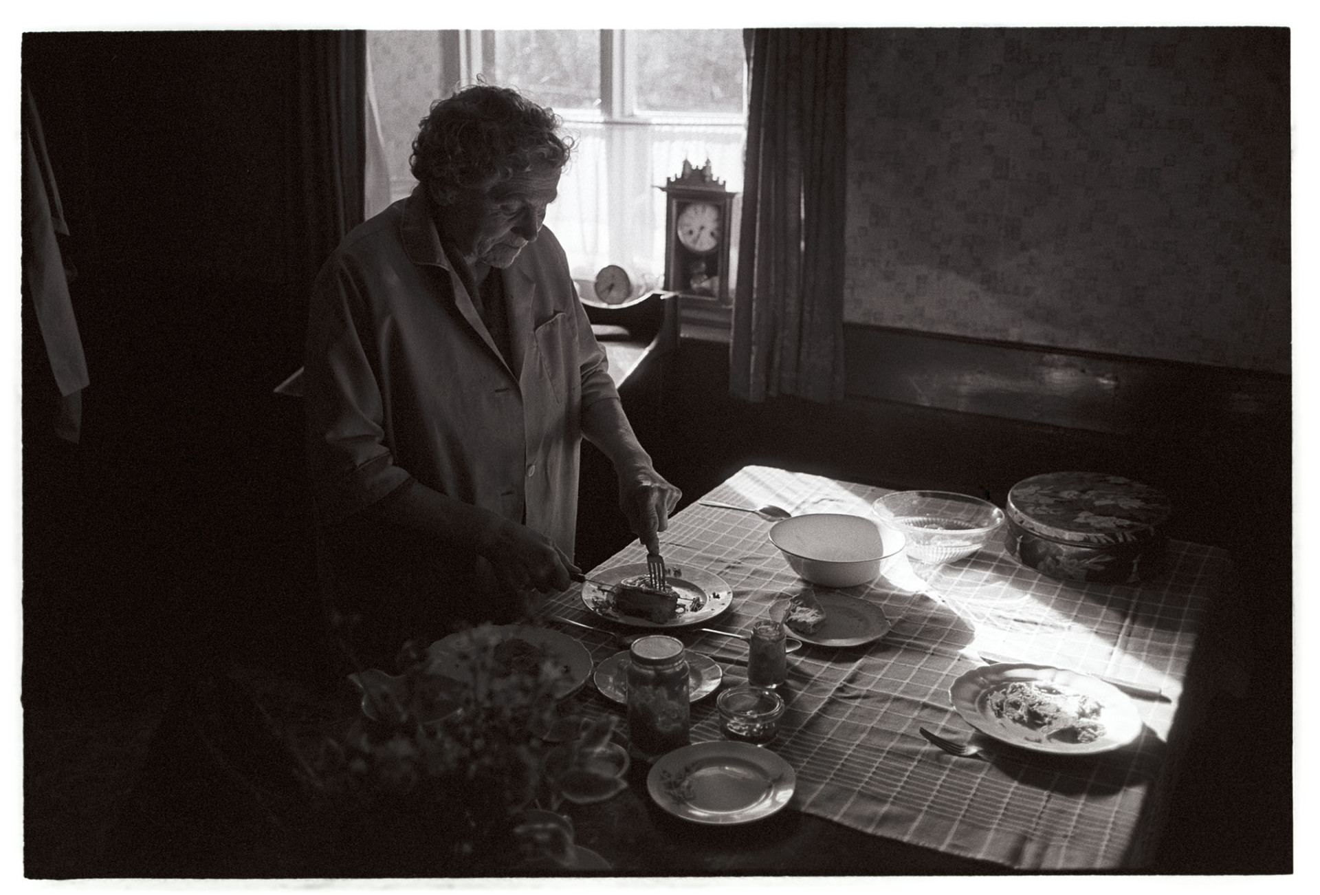 Woman cutting ham for lunch at table. Meal.
[Mrs Hatherley standing at a table, set for a meal, cutting meat on a plate with a knife and fork at Meeth.]