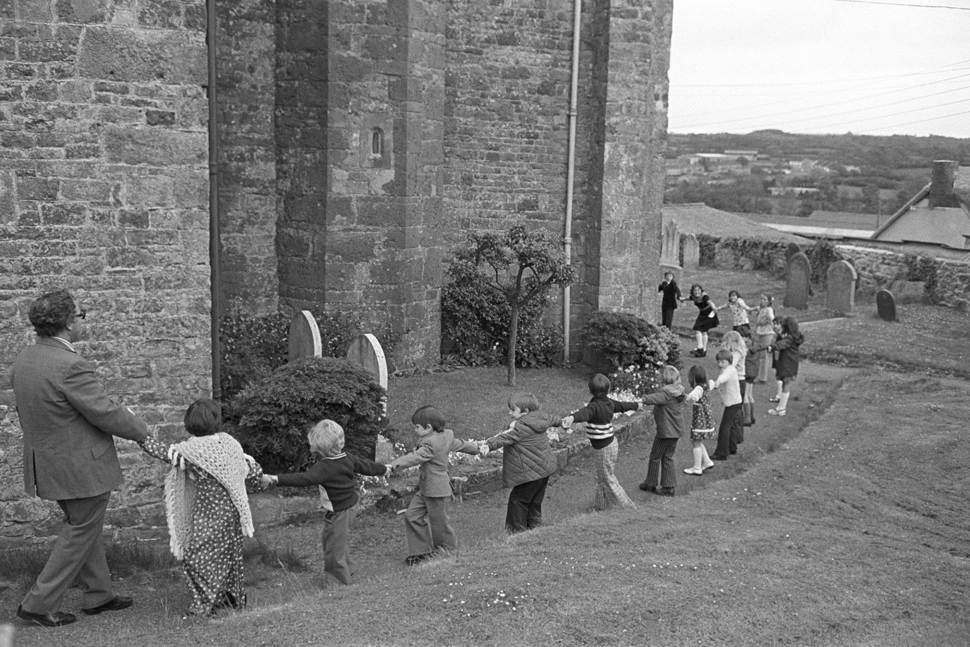 Girdling church after parade Headmaster pulling.
[Charles Tucker with children holding hands around Hatherleigh church for the Church Sunday School Parade.]