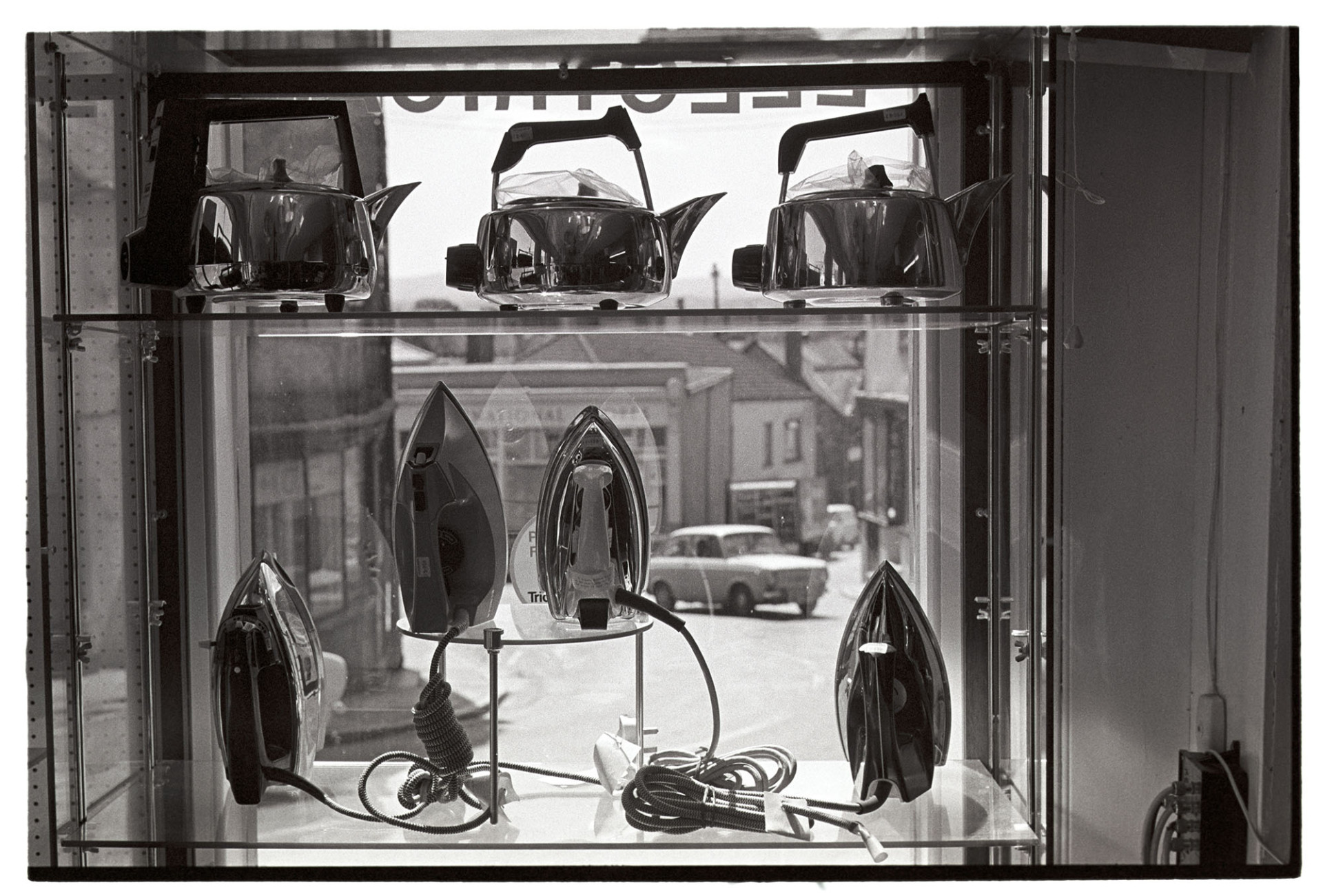 Goods in window of electrical shop, kettles, irons.
[A display of kettles and irons in the window of Hockin's electrical shop, Market Street, Hatherleigh.]