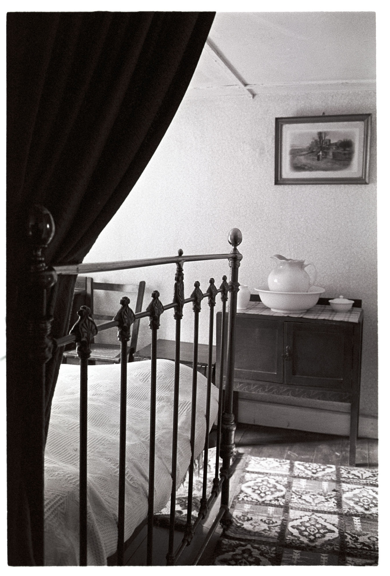 Bedroom interior, washstand  and bedstead.
[A bedroom at Millhams, Dolton, with a washstand and a wrought iron bedstead. Possibly in Archie Parkhouse's house.  A picture hangs on the wall above the washstand.]