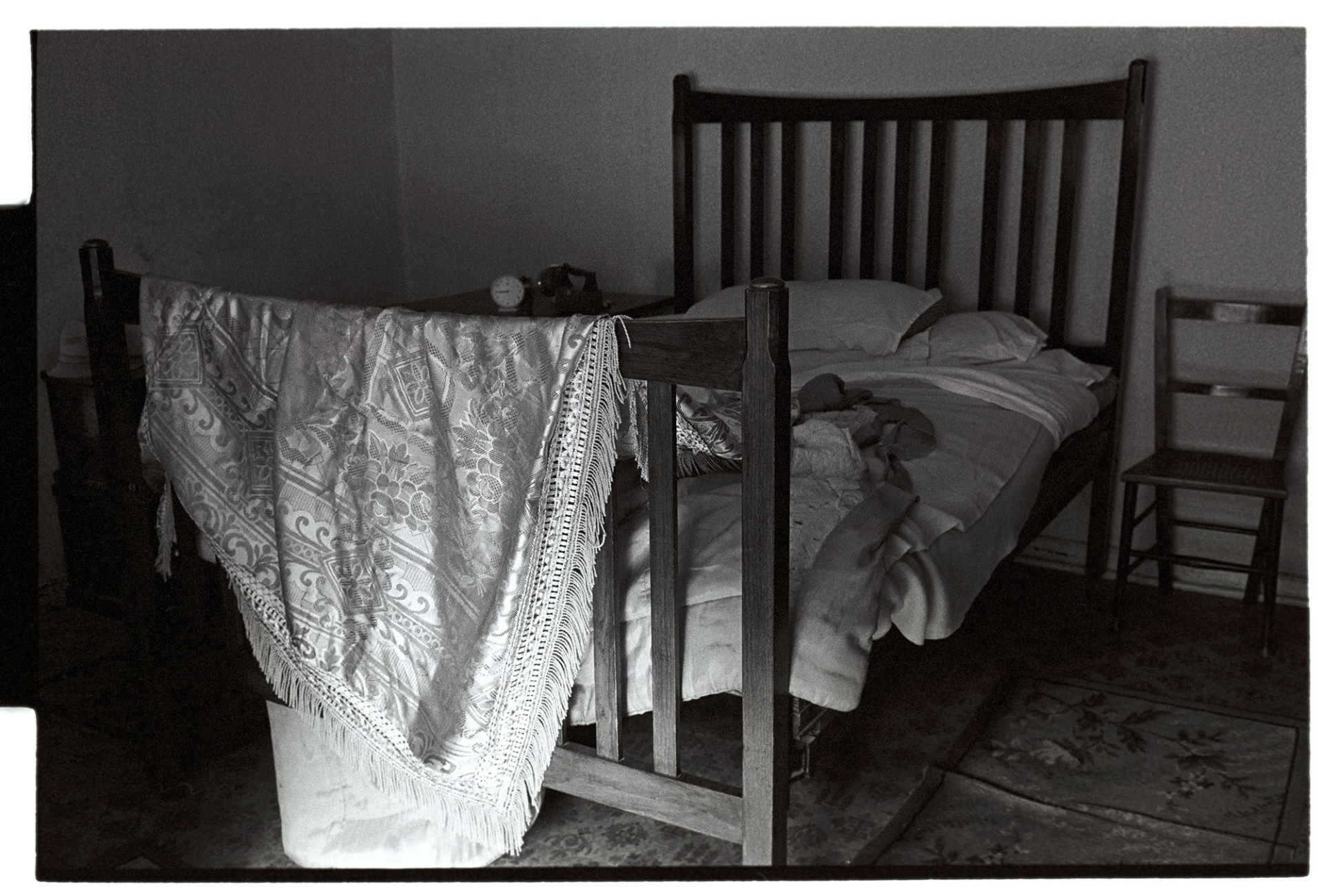 Bedroom interior, unmade bed and counterpane.
[An unmade bed with a counterpane or bedspread hanging over the wooden bedstead in Archie Parkhouse's bedroom at Millhams, Dolton.]