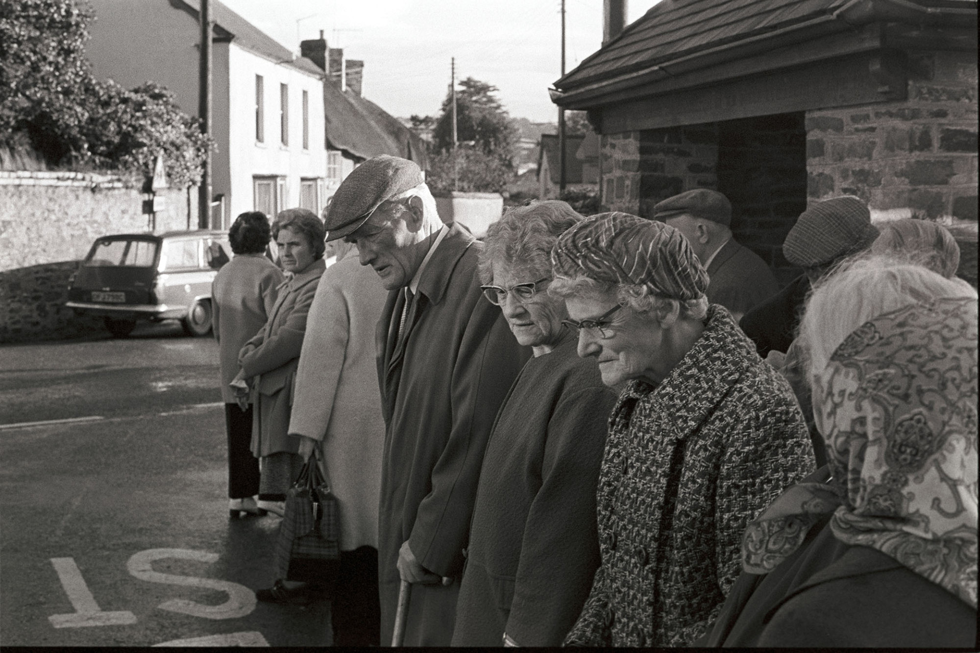 Over 60's club members about to go on bus outing, waiting in queue.
[A group of men and women from an Over 60's Club, standing in line at the bus stop in Dolton, waiting to go on a day trip.]