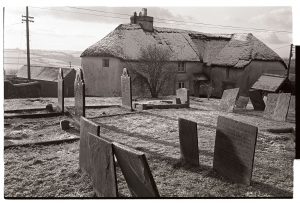 Graveyard with thatched farmhouse by James Ravilious