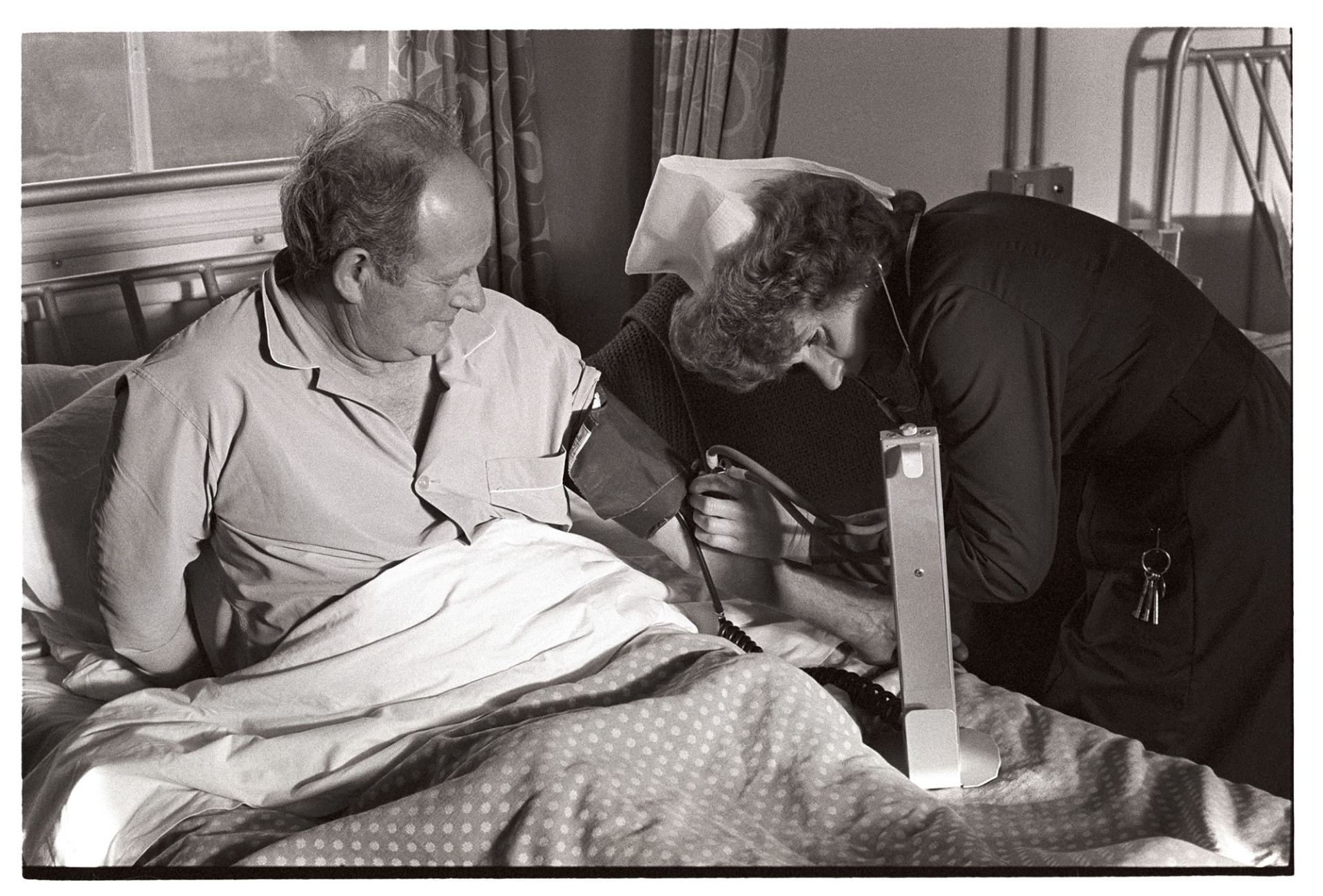 Hospital nurse taking man's blood pressure on Christmas Day.
[A nurse taking a the blood pressure of a patient in his bed at Torrington Cottage Hospital on Christmas Day.]