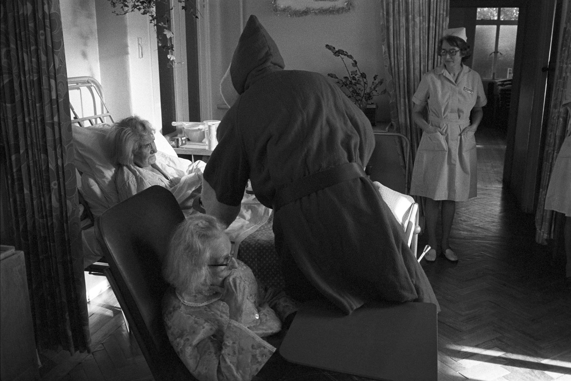 Doctor as Father Christmas in hospital ward, Christmas Day, reassuring woman patient.
[Dr Cramp dressed as Father Christmas visiting patients on the ward in Torrington Cottage Hospital with a nurse standing watching.]