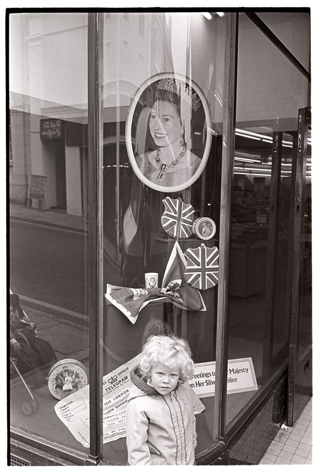 Girl outside shop with display for Jubilee.
[The shop window of F W Woolworths in Bideford High Street decorated for Queen Elizabeth II's Silver Jubilee.  A child is standing by the window.]