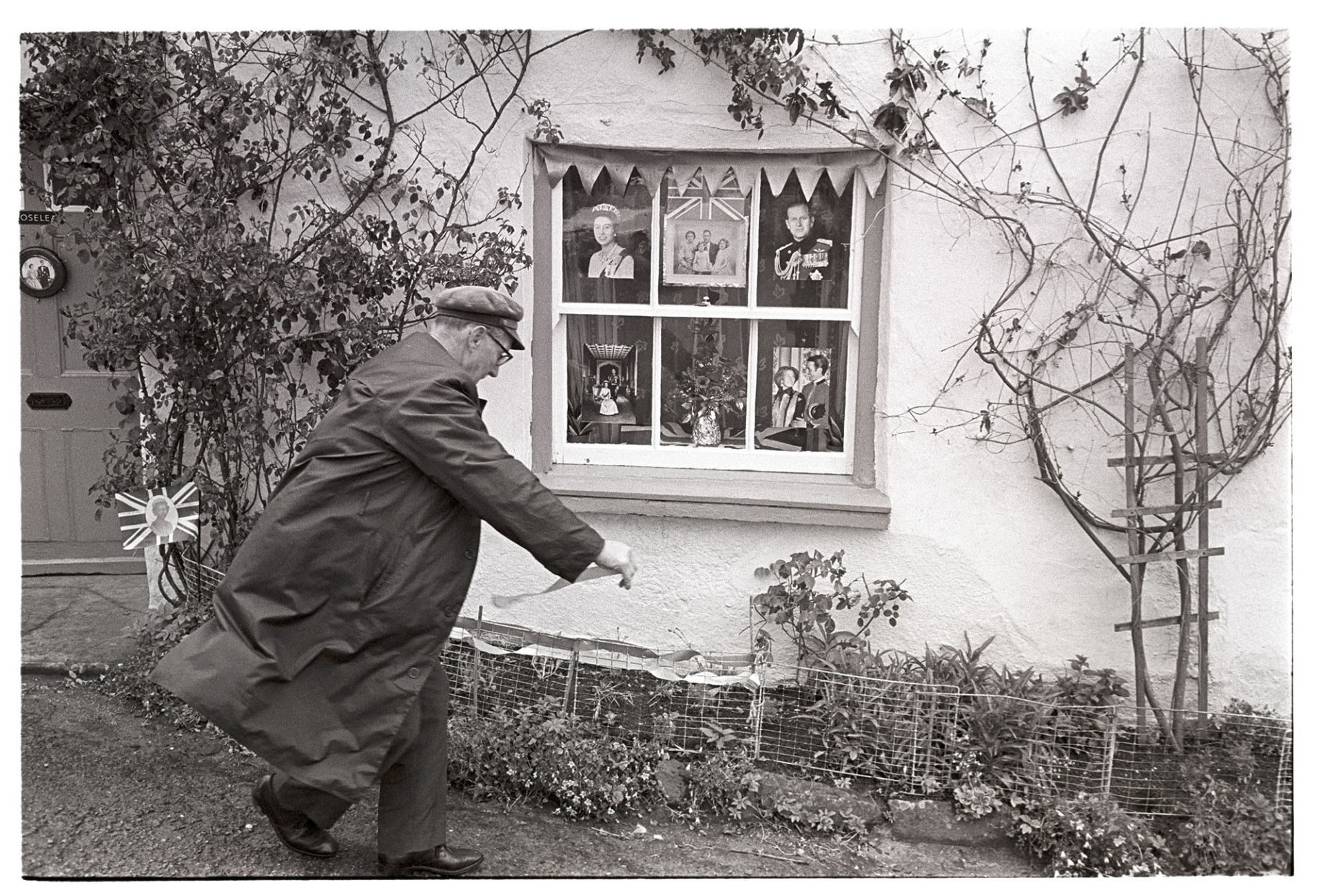 Man decorating house for Jubilee.
[Jack Marden decorating his house and garden at Rose Cottage, Aller Road, Dolton for the Silver Jubilee of Queen Elizabeth II. There are photographs and bunting in his window.]