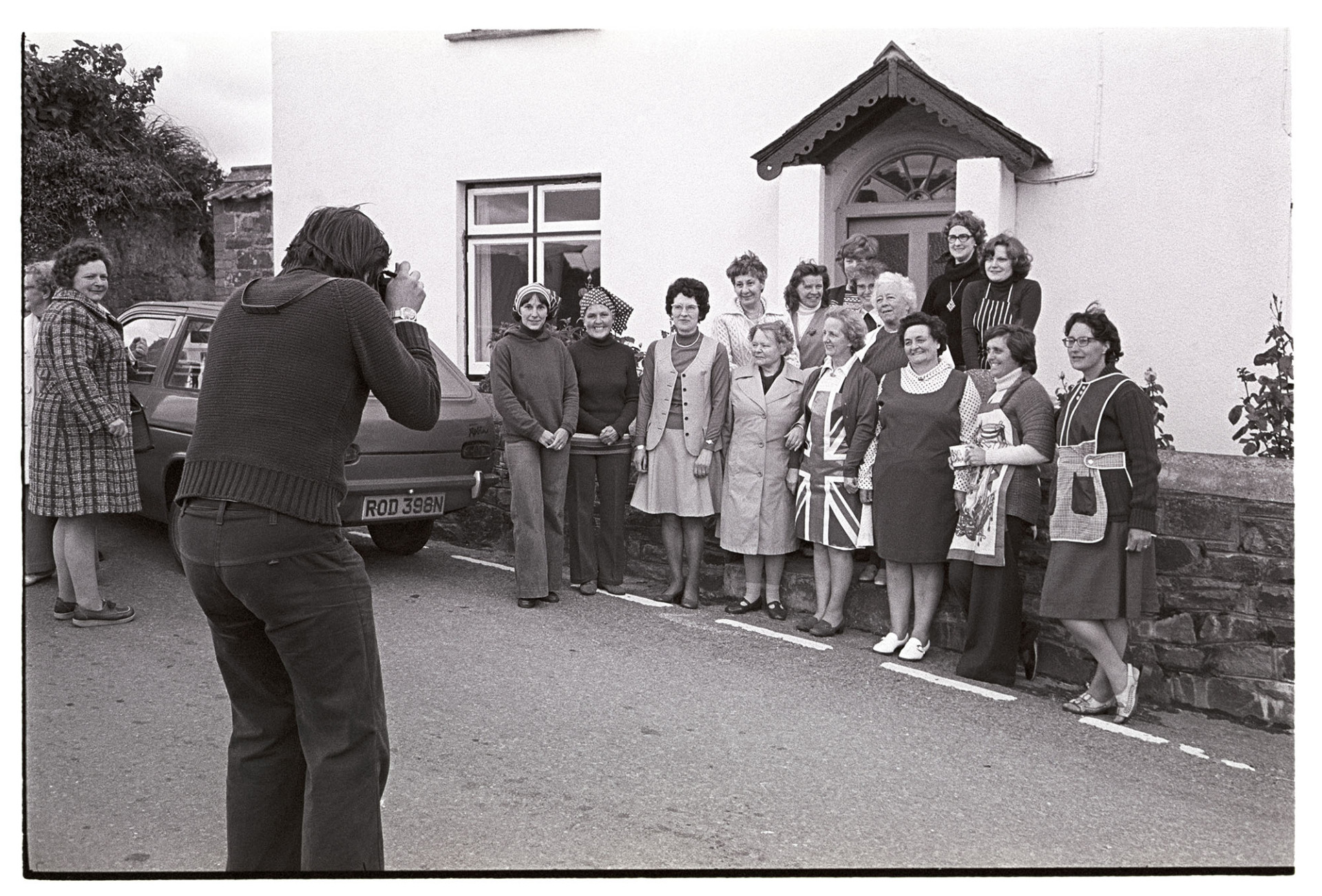 Group of women organisers who worked, photographer taking their photograph.
[Chris Hammond taking a photograph of women gathered outside a cottage in Atherington. They had arranged the celebration for the Silver Jubilee of Queen Elizabeth II in the village.]