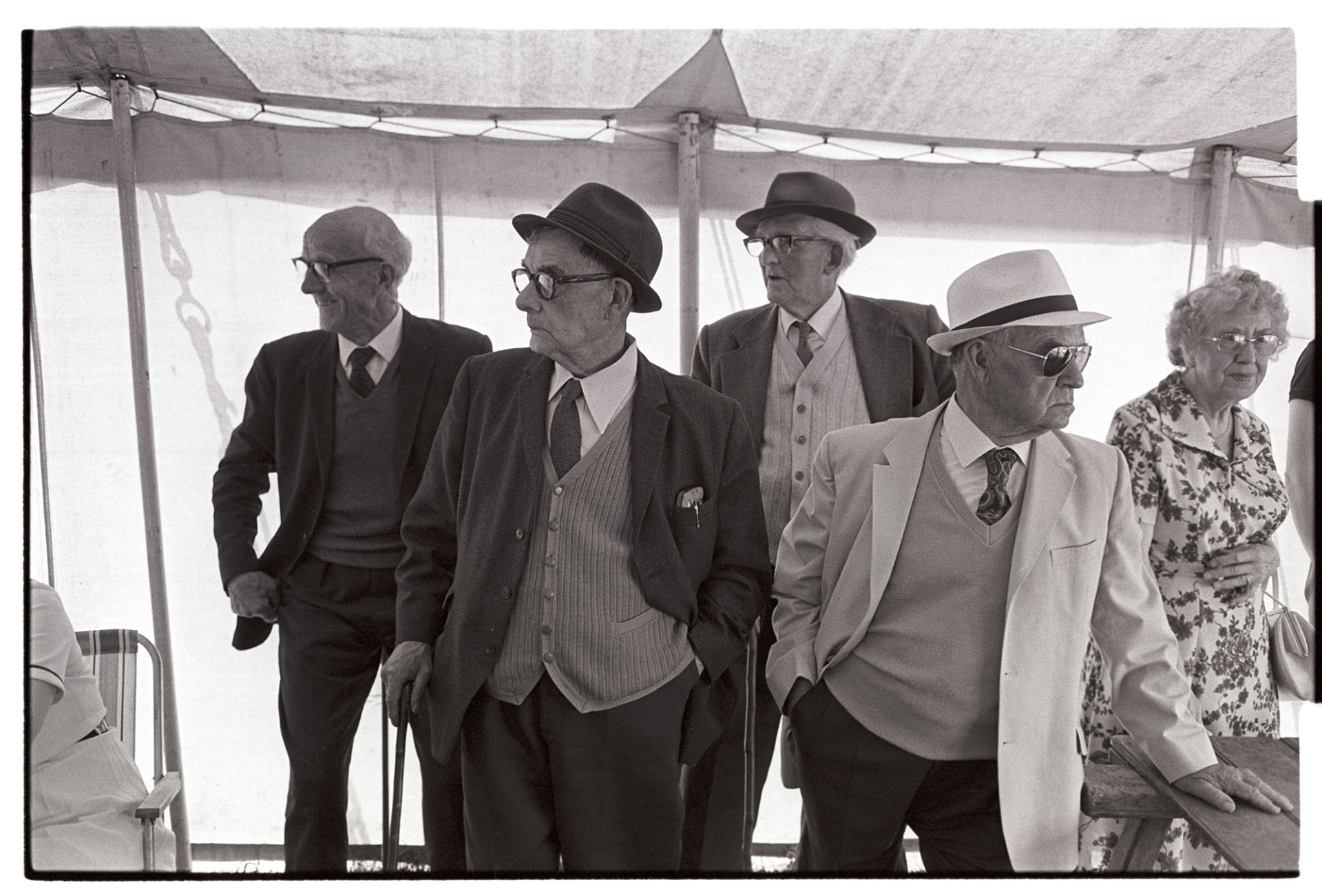 Fete, spectators in tent, hats. 
[Four men and a woman in a tent or marquee at Marwood Village Fete. Three of the men are wearing hats.]
