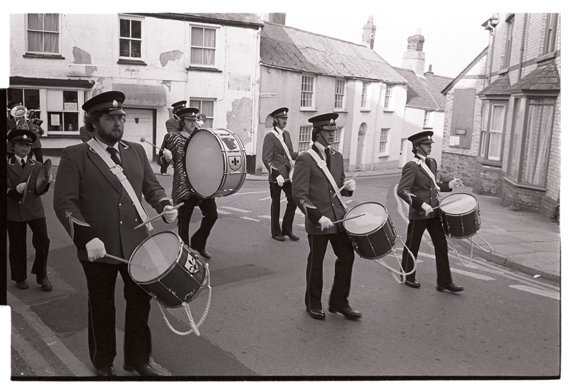 Military parade round town, the Brass Band corps of drums.
[Members of a  Corps of Drums playing and marching in a street in Torrington at a military parade.]