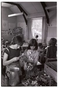 Children arranging flowers in classroom by James Ravilious