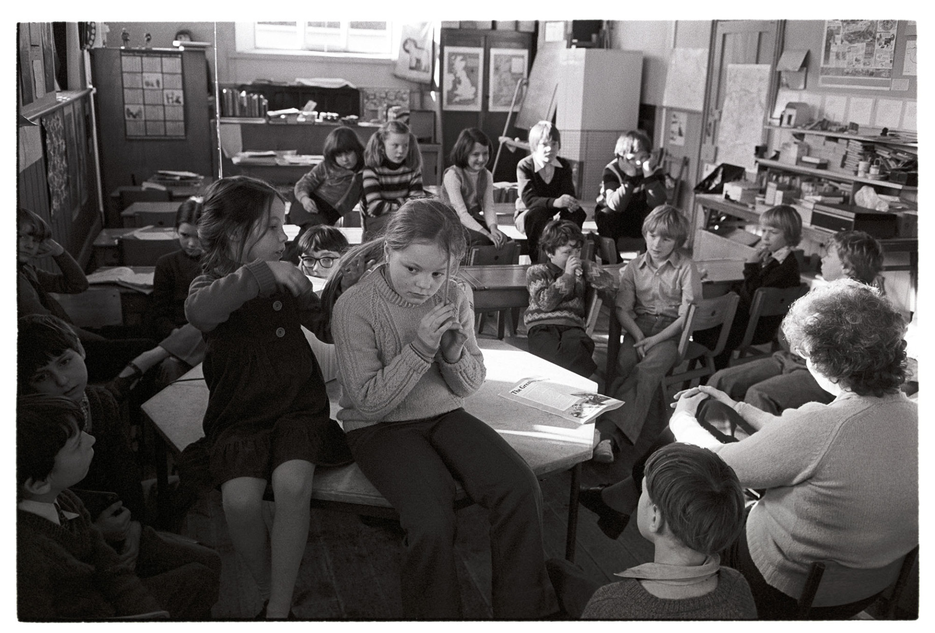 Primary school classroom with children listening to radio, girl doing friends hair!
[Schoolchildren at Burrington Primary School listening to a radio broadcast in a classroom. One girl is sat on a table and styling her friends hair.]