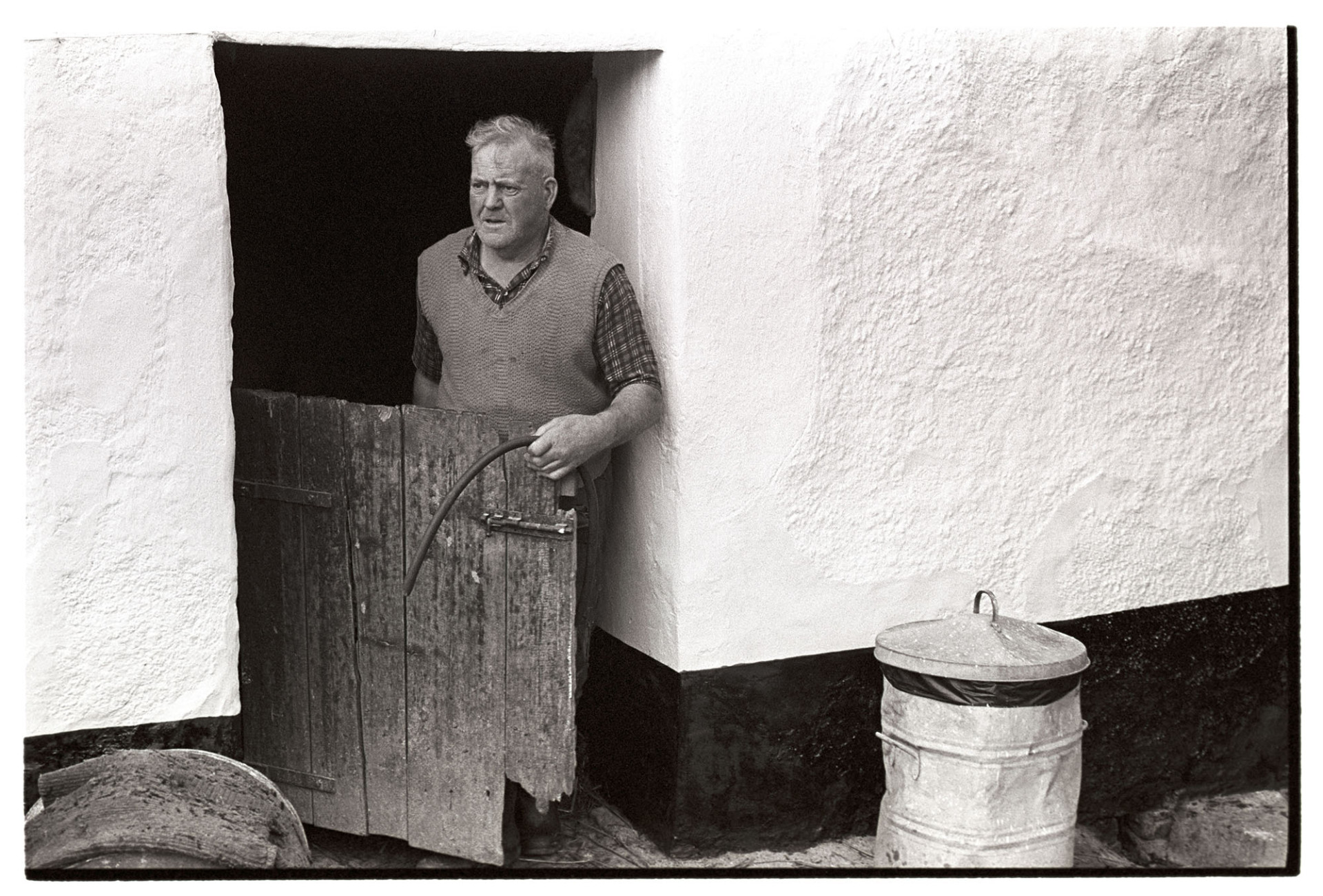Farmer at doorway to milking shed. 
[Cyril Bennett stood by the wooden doorway of the milking shed or parlour at Cuppers Piece, Beaford.]