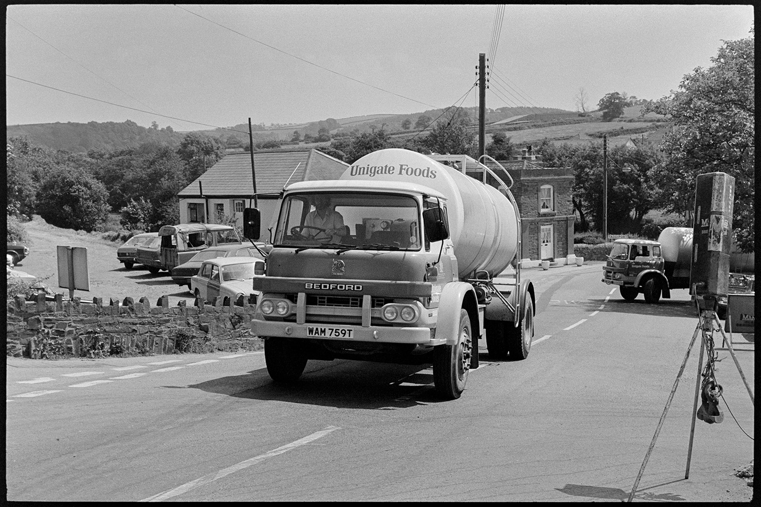 Lorries with milk churns, men unloading, checking, sniffing and weighing milk, lorry parked. 
[A milk tanker on a road in Torrington, possibly after leaving the Unigate Dairy milk factory in Torrington.]