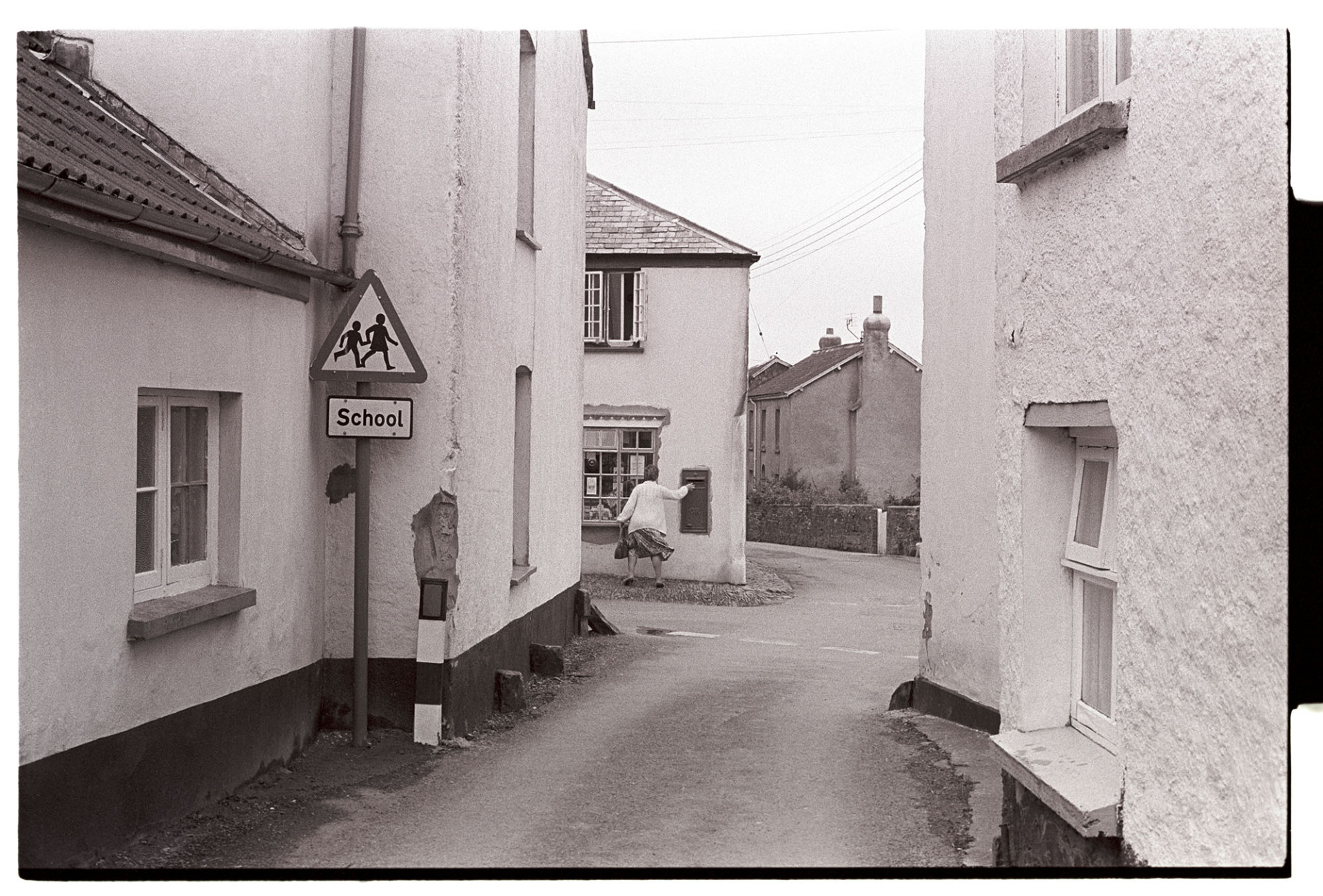 Street scene woman posting letter. 
[A street view in High Bickington with a road sign and a woman posting a letter in a post box, possibly at High Bickington Post Office.]