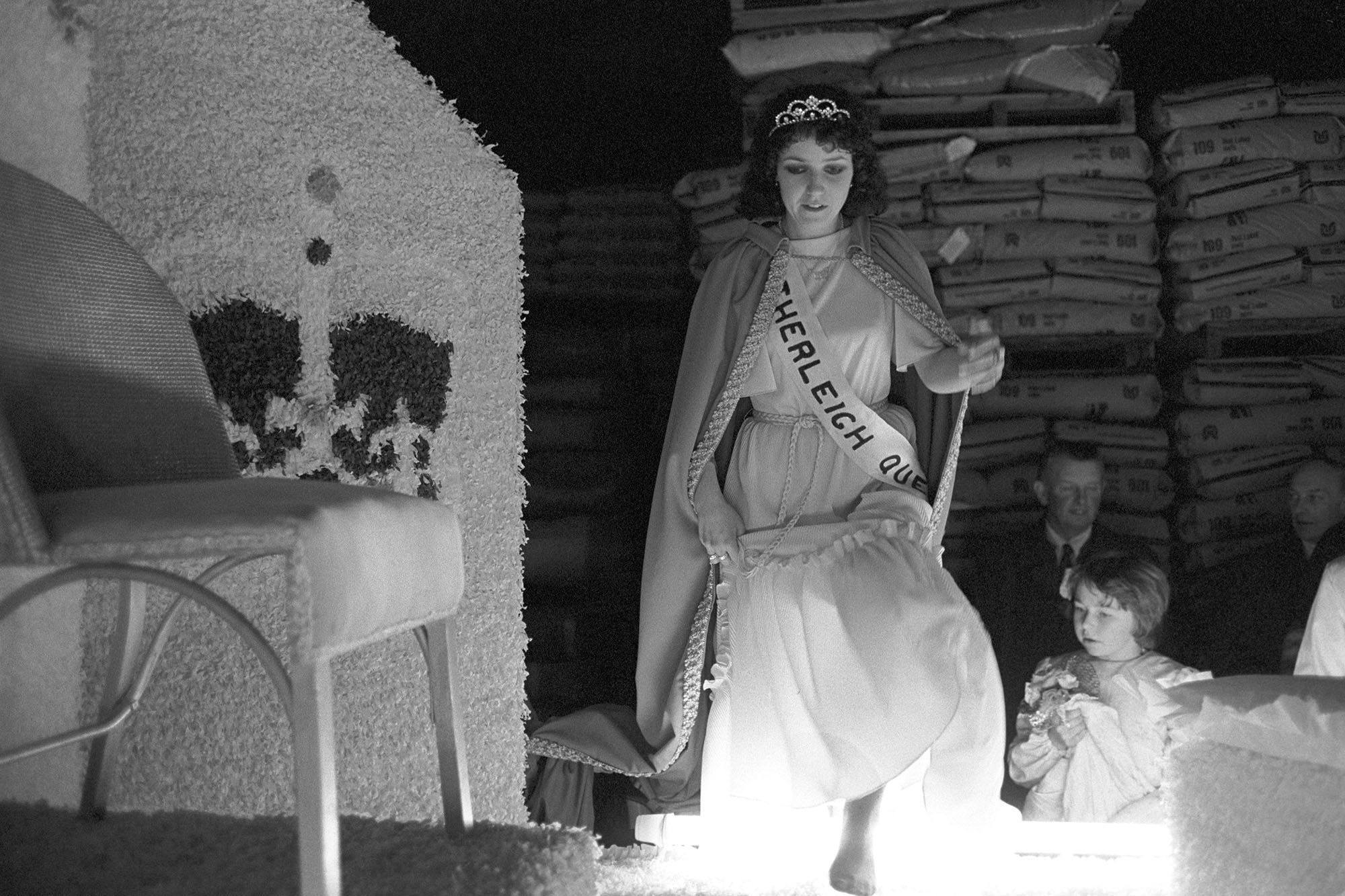 Carnival Queen stepping up to her throne at night. 
[Cindy-Jane Dillon, Hatherleigh Carnival Queen stepping up to her throne on a carnival float at Hatherleigh Carnival at night.]