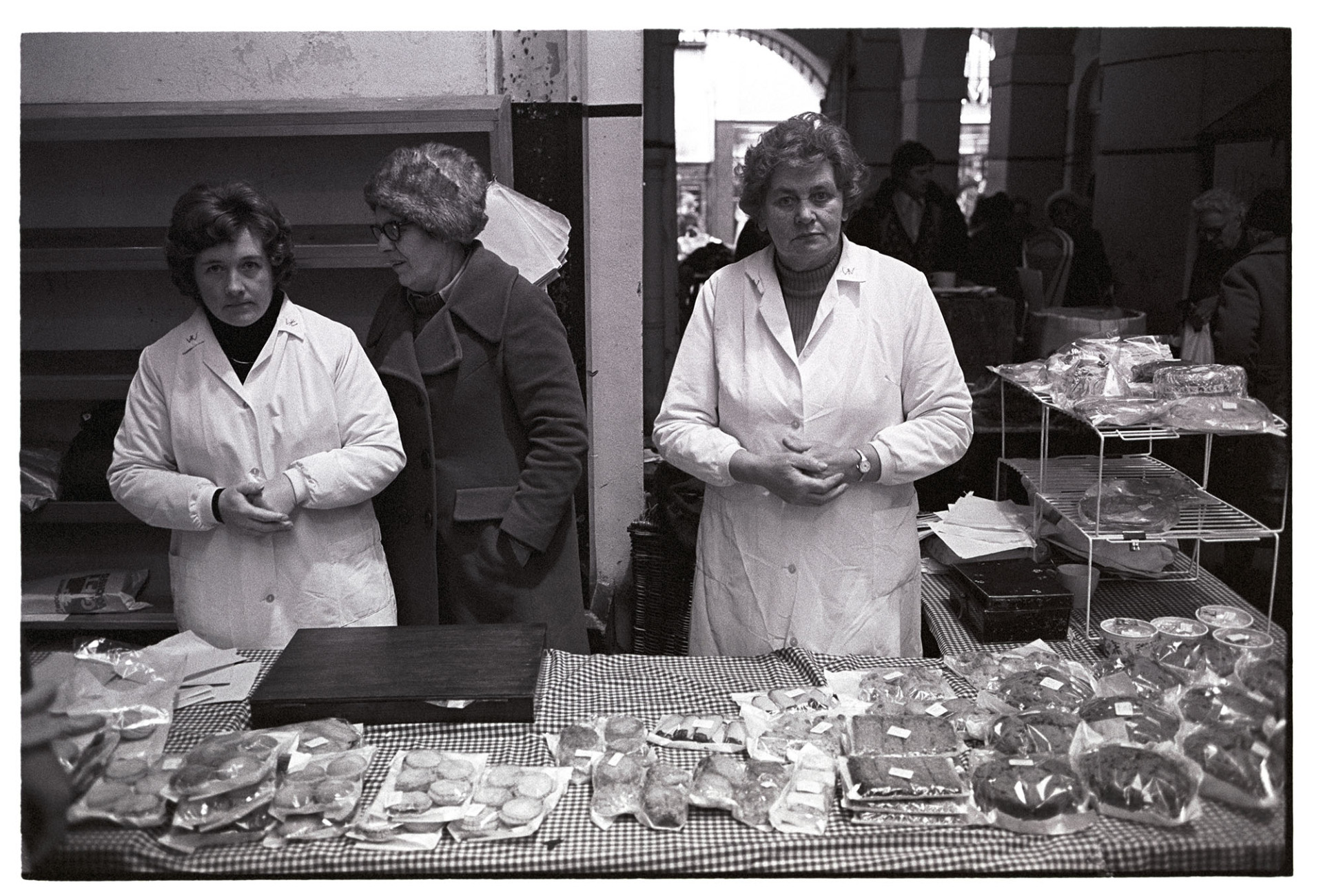 Stall at Pannier Market. Women's Institute cake stall. 
[Rene Ware, stood on the right, and another woman serving on the Women's Institute cake stall at Barnstaple Pannier Market.]