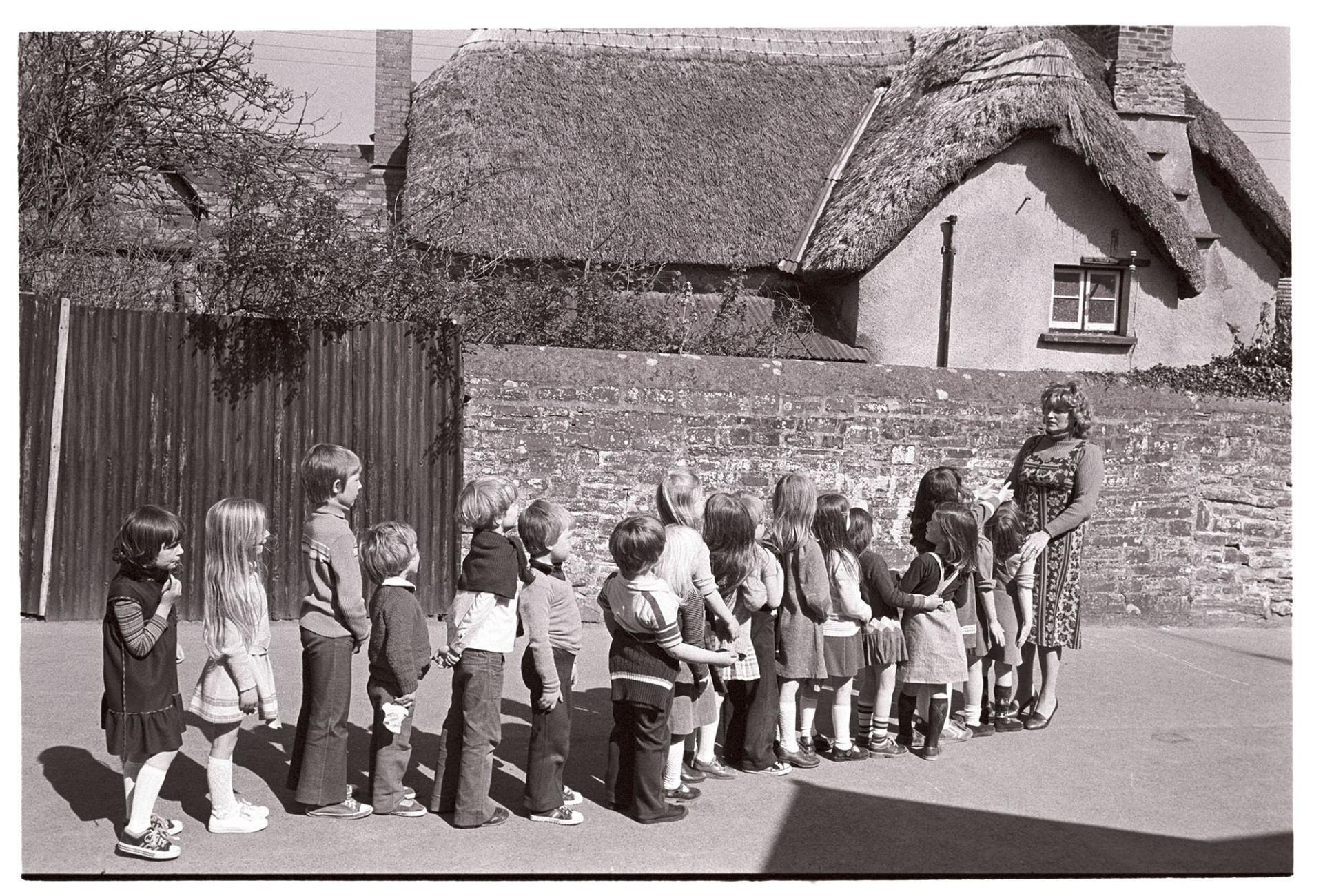 Primary School children lined up in yard with teacher. <br />
[Children lined up in front of their teacher, Sheila McCulloch in Dolton Primary School playground. The fifth child from left is Ben Ravilious. A thatched cottage is in the background.]