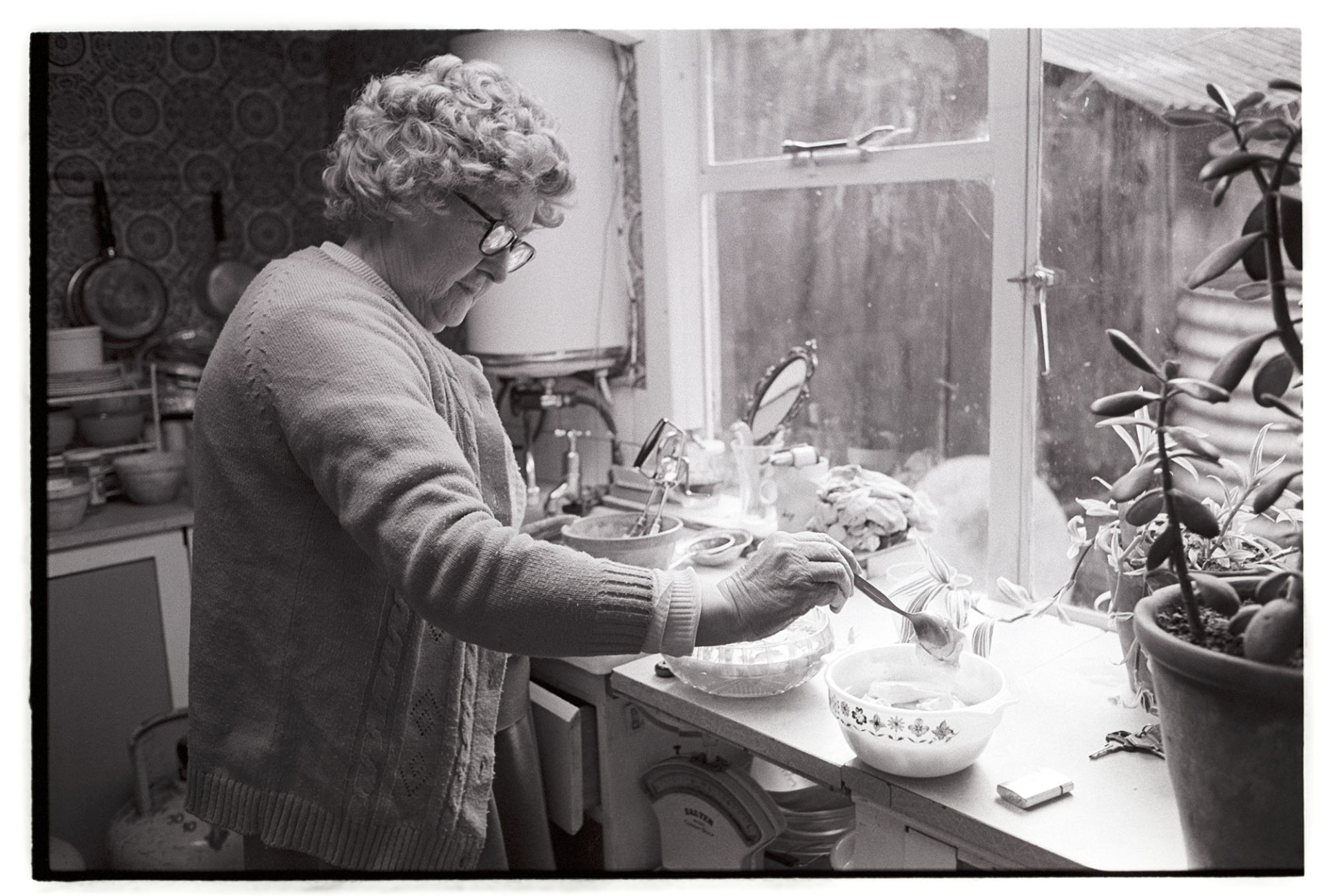 Woman making trifle, adding custard, wearing wig. 
[Mrs Hutchins adding custard to a trifle she is making in her kitchen in Dolton. She is wearing a wig.]