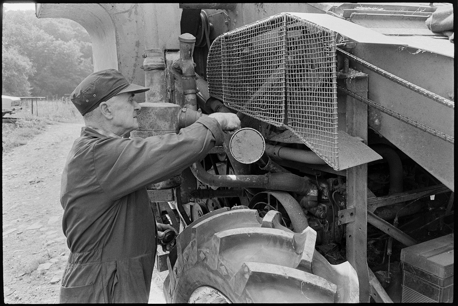 Agricultural engineers workshop, mending puncture, tractors, combine harvester. 
[A man oiling a combine harvester at an agricultural engineer's premises at Hollocombe.]