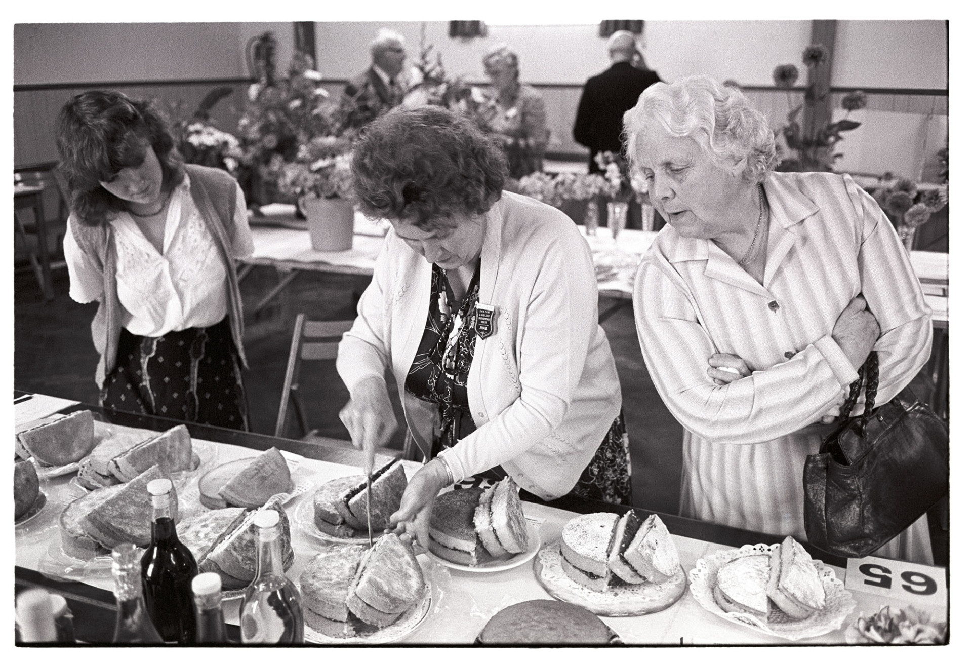 Woman judging cakes at Dolton Flower Show by James Ravilious
