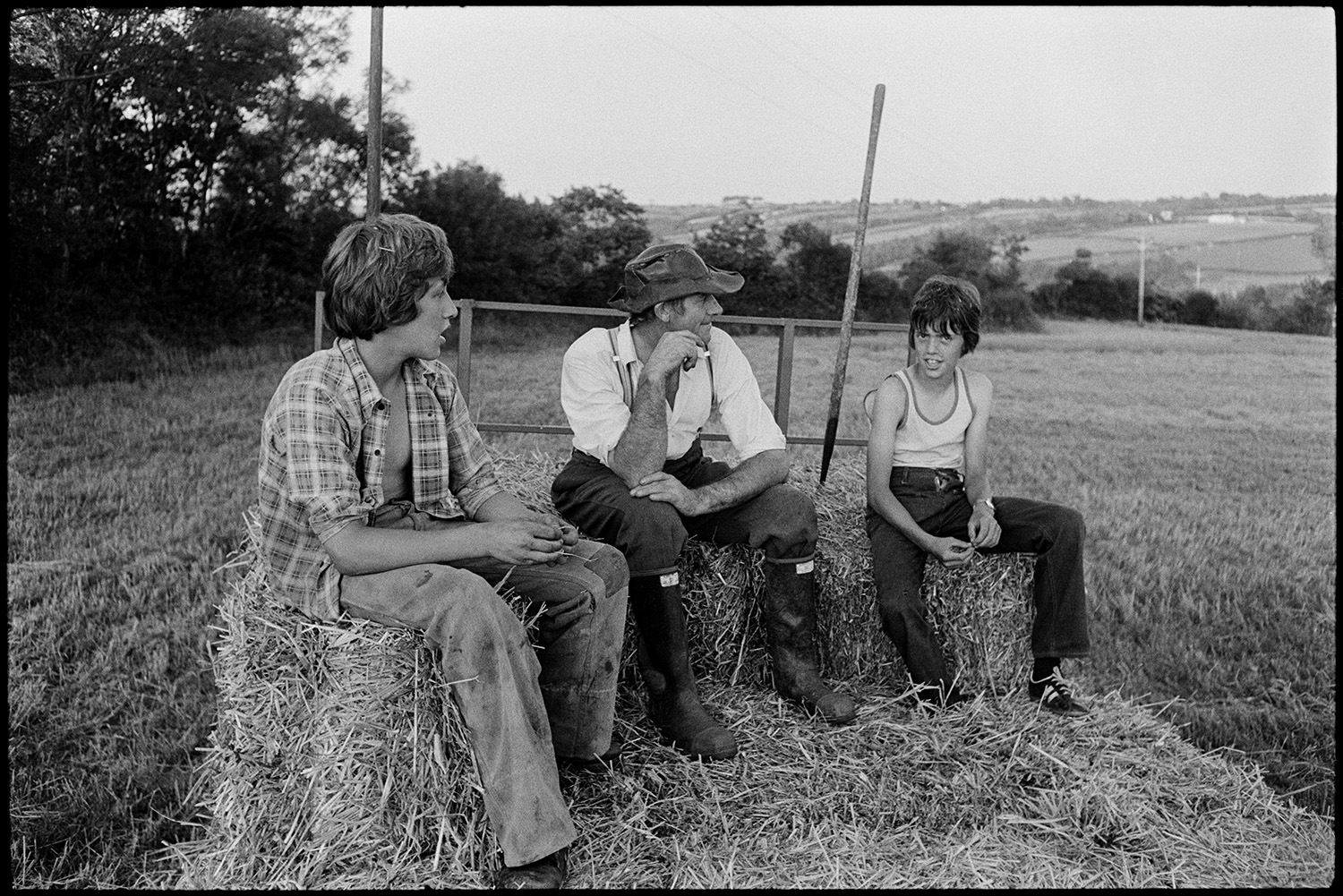 A man and two boys sat on straw bales on a trailer in a field at Hollocombe.