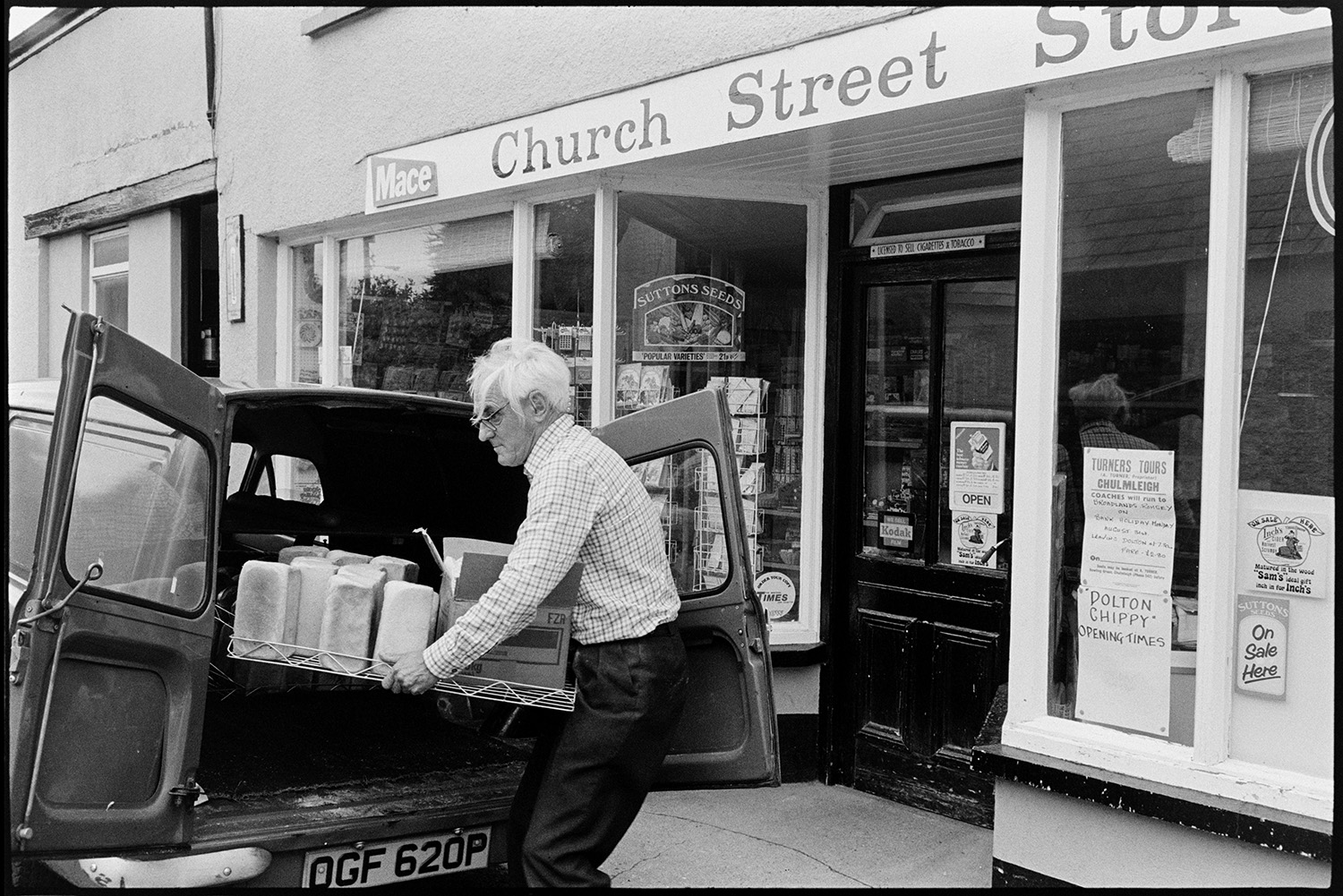 Baker delivering bread to village shop, loaves. 
[A baker delivering a tray of loaves of bread, from a van, to Church Street Stores in Church Street, Dolton.]