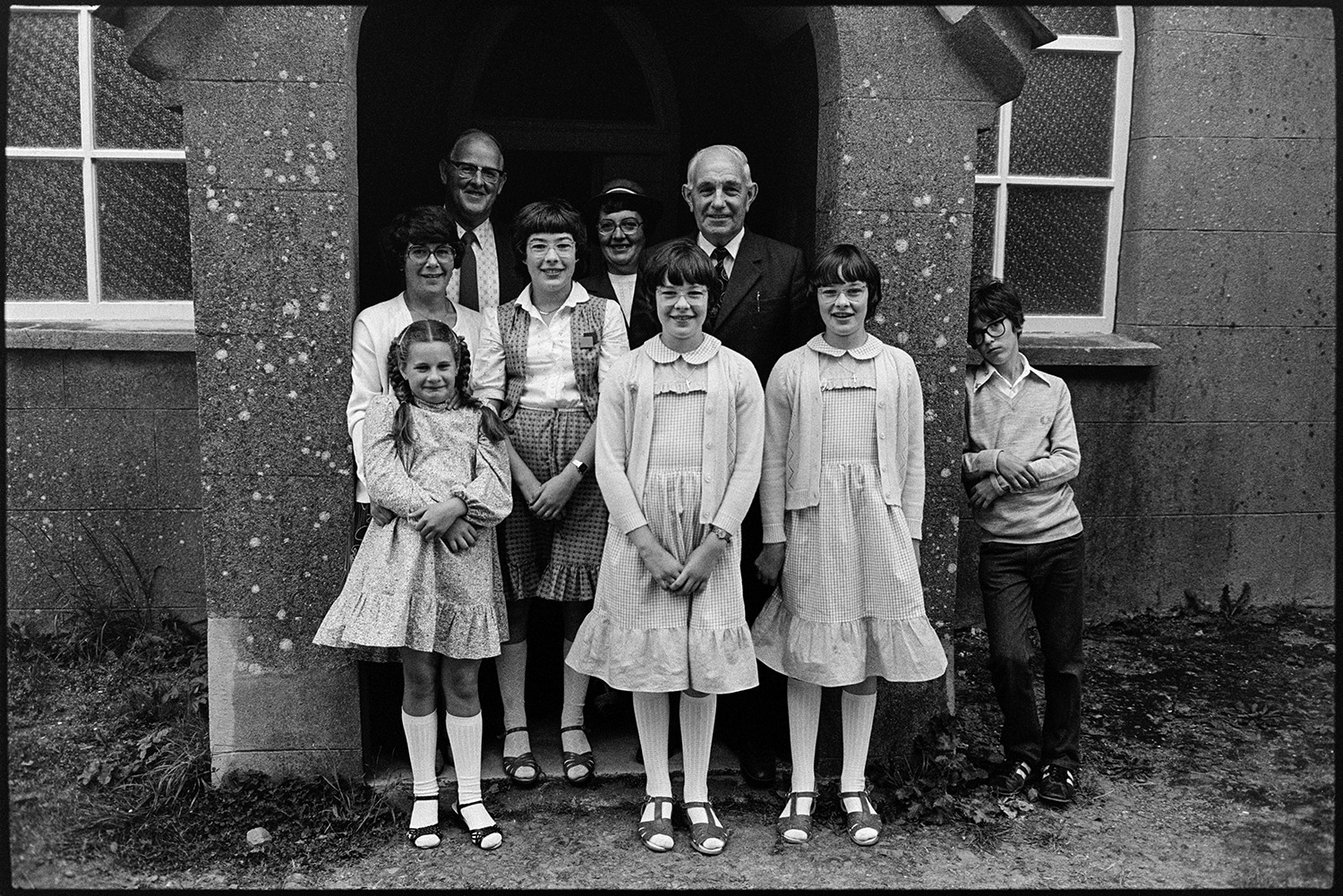 People posing after Chapel service, congregation. 
[A small group of men, women and children posing at the entrance to Langham Chapel after a service.]
