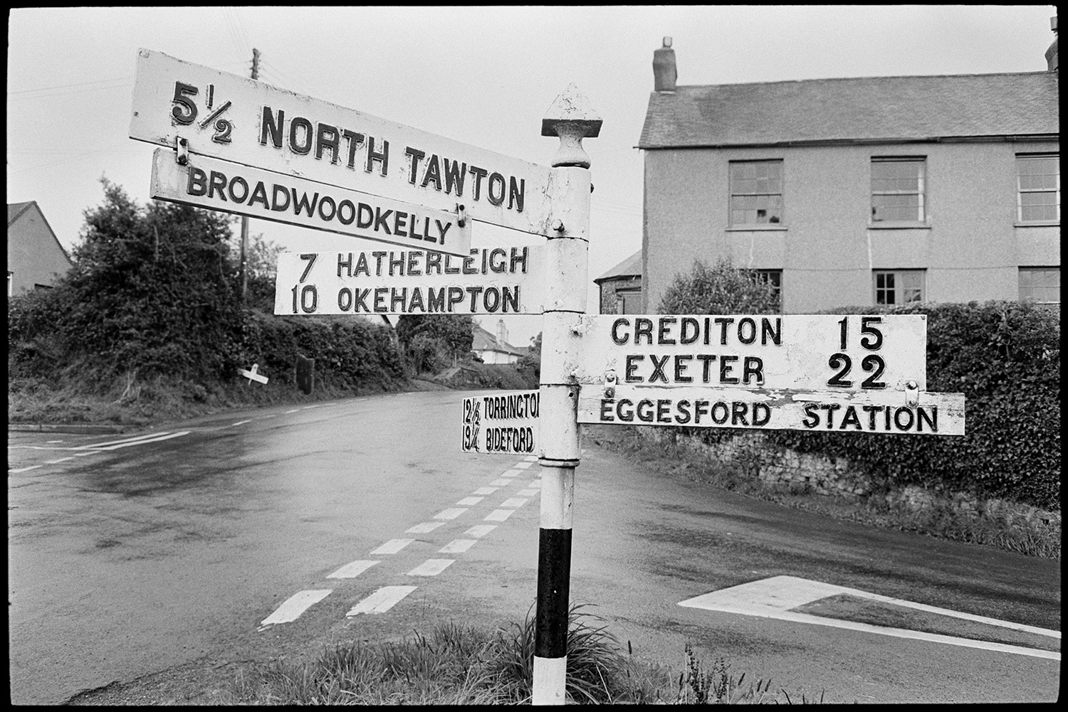 Road sign, lots of names. <br />
[A signpost pointing in many directions at a wet crossroads in Winkleigh with house in the background.]