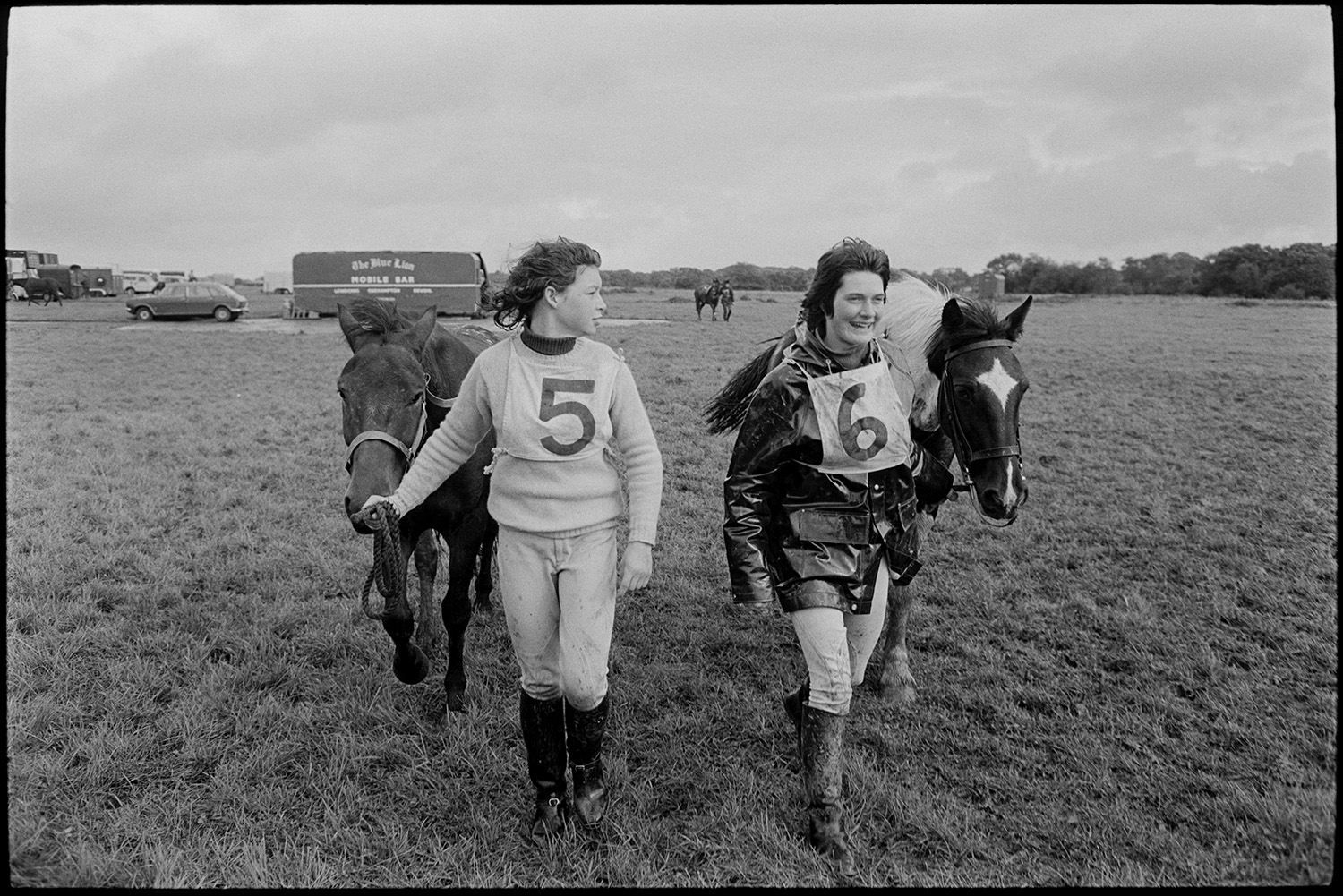 Competitors with horses at Steeplechase.
[A woman and a girl leading horses across Winkleigh Aerodrome, after taking part in a steeplechase. Vehicles and horse boxes are visible in the background.]