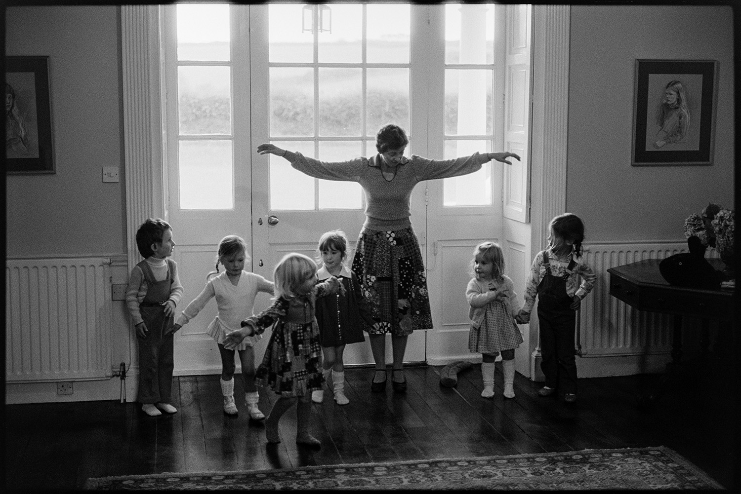 Children's dance class in large country house. Teacher.
[A woman teaching a dance class to children at Marwood House, by a large doorway.]