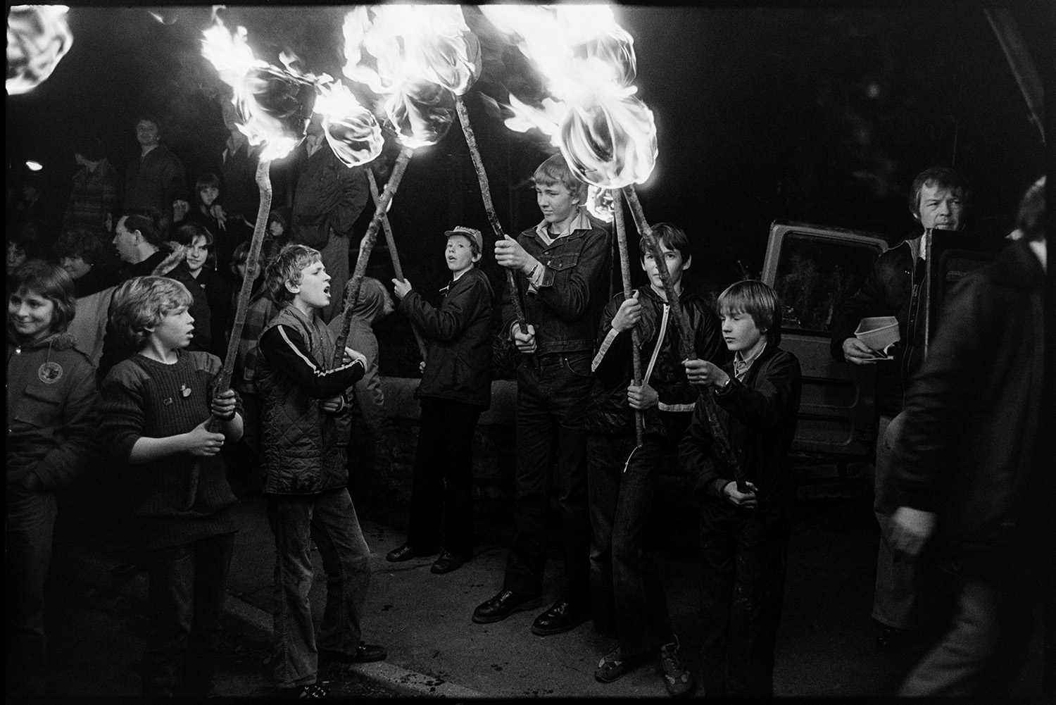 Carnival floats at night people in fancy dress, flares, Bride and Groom. 
[A group of boys holding flaming torches at Dolton Carnival.]