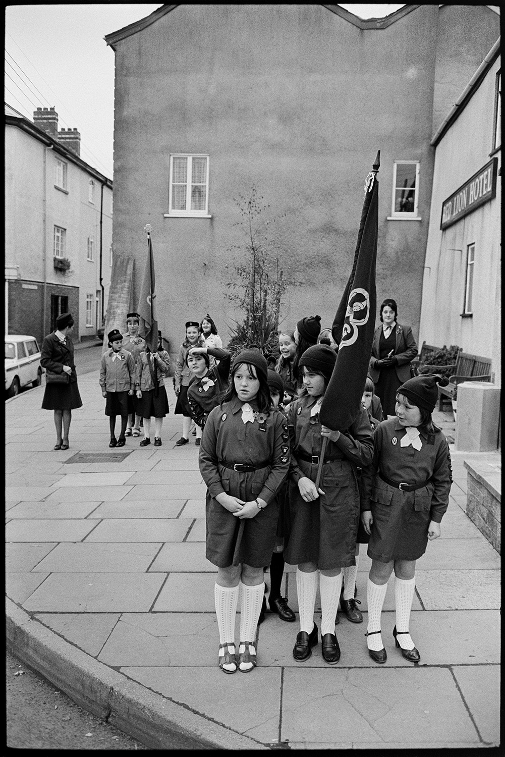 Armistice Day, inspection and parade to church, both women and men. Scouts and brownies. 
[Groups of brownies lined up for the Remembrance Day parade in Chulmleigh. Two of them are carrying flags.]
