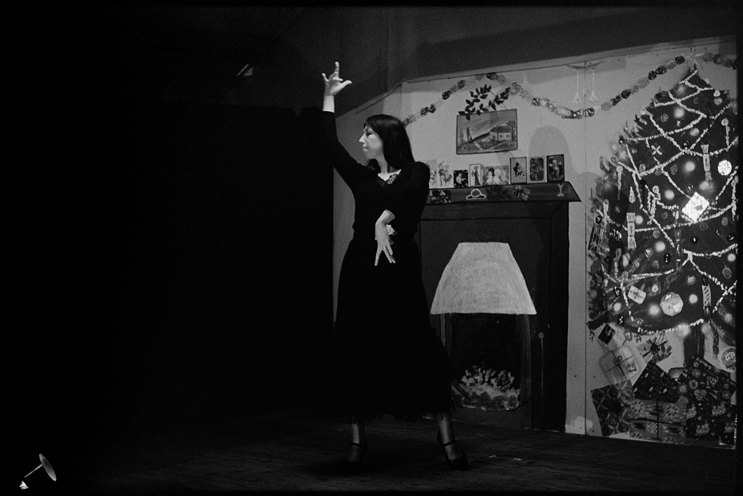 Christmas entertainment in village hall, singing and dance, short plays.
[A woman dancing against a backdrop of a fireplace and Christmas tree on stage at High Bickington village hall at an evening of Christmas entertainment.]