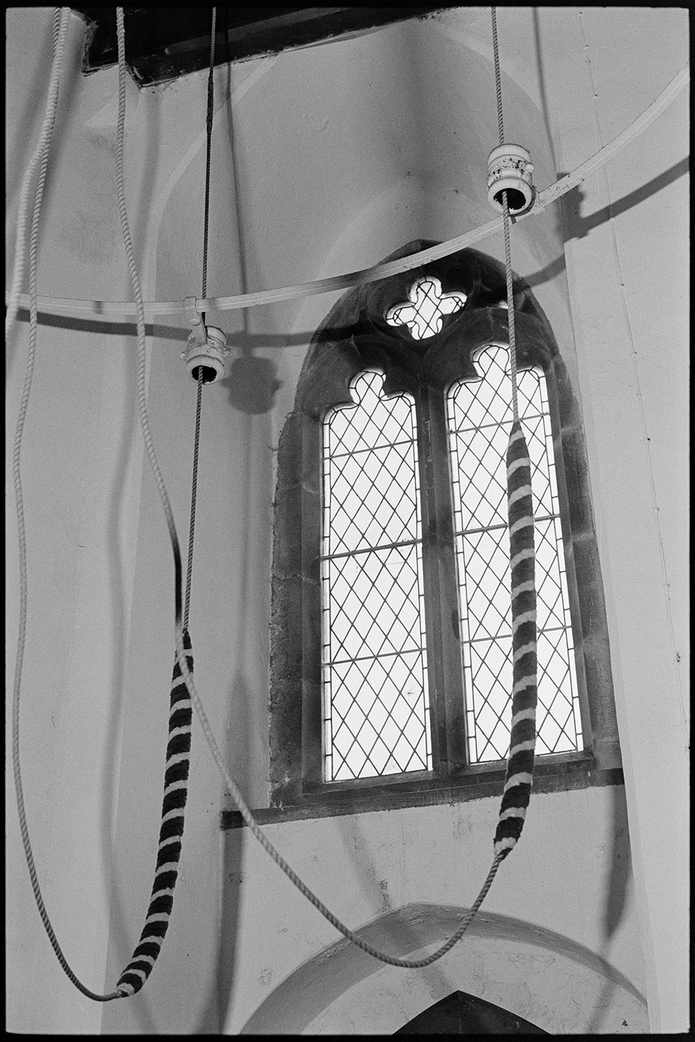 Church interior with bell ropes.
[ The interior of Brushford Church showing bell ropes and an arched window.]
