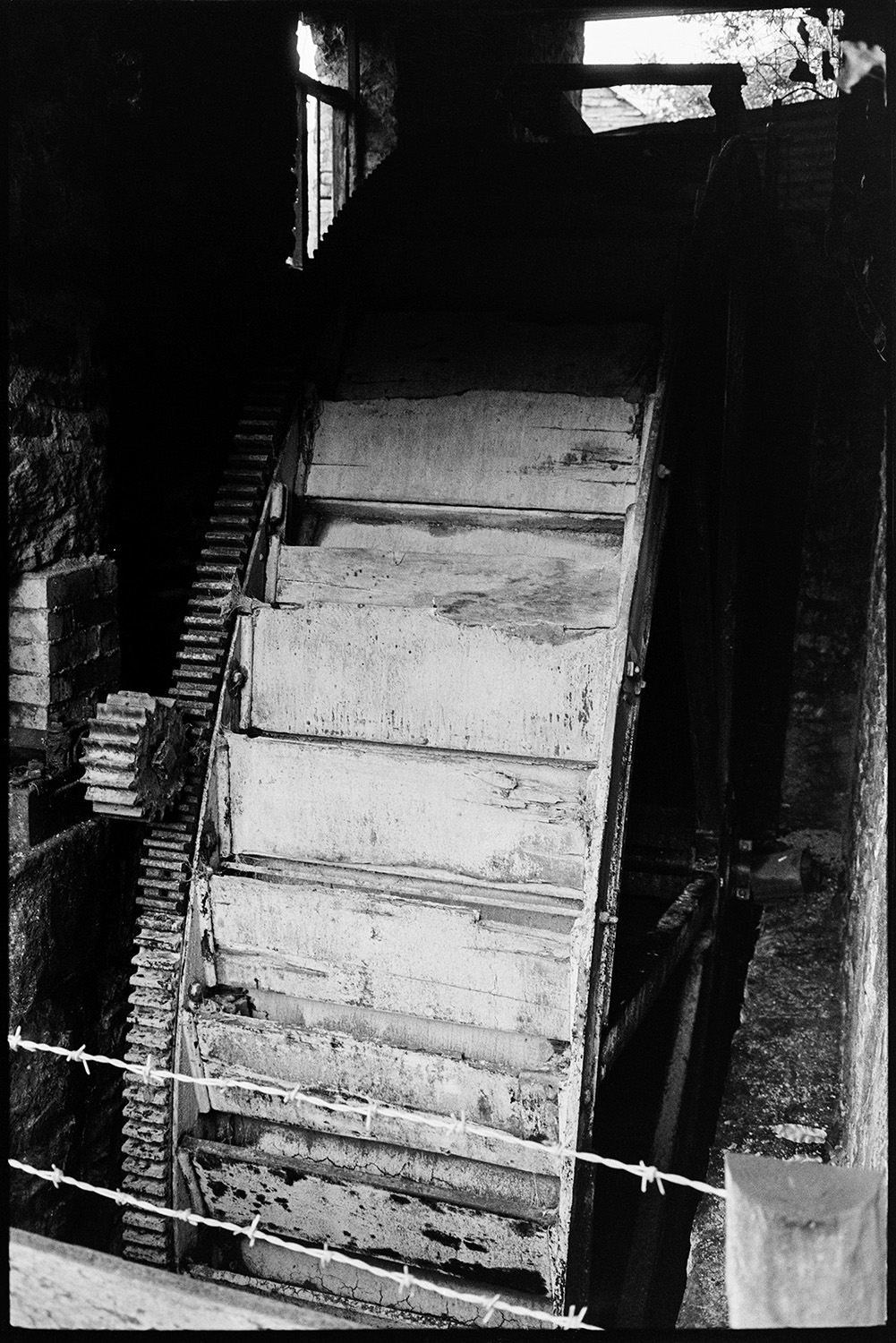 Mill wheel, undershot.
[Old mill wheel and undershot in a shed at West Chapple Farm near Winkleigh. Barbed wire is visible in the foreground.]