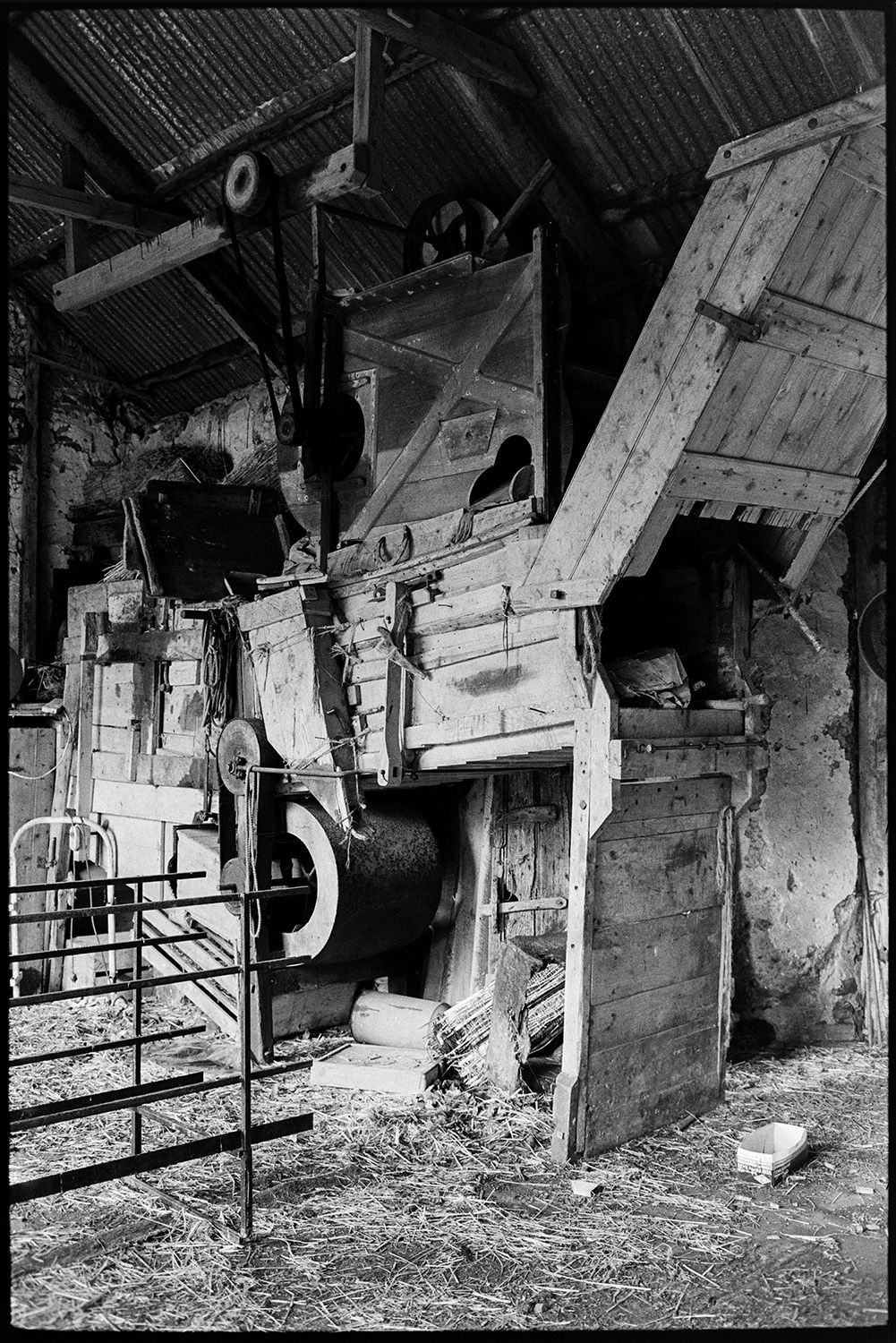 Barn thresher, threshing machine.
[Old wooden threshing machine in a barn with a corrugated iron roof at West Chapple Farm, near Winkleigh.]