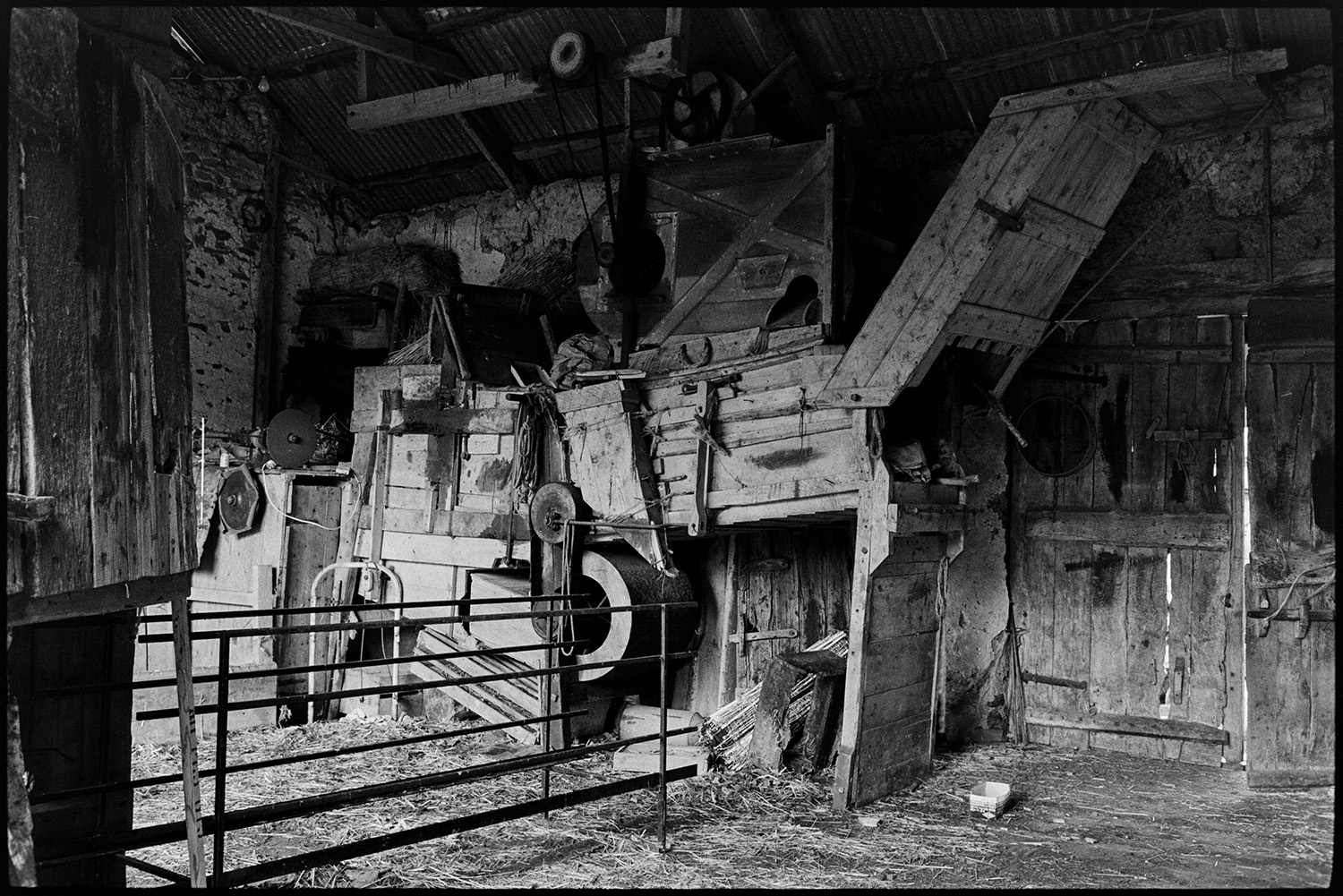 Barn thresher, threshing machine. 
[An old wooden threshing machine in a barn with a corrugated iron roof and a wooden door, at West Chapple Farm, near Winkleigh