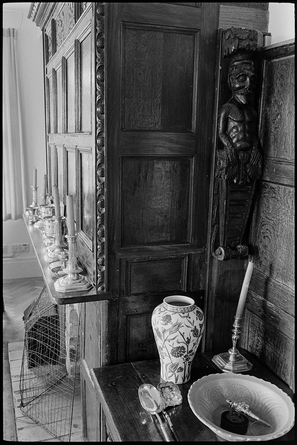 House interior with furniture, paintings, harpsichord, panelled screen, china.
[Interior of a room in a house in Dolton belonging to Michael Davis, showing a wood panelled wall with carving, candlesticks and a china vase.]