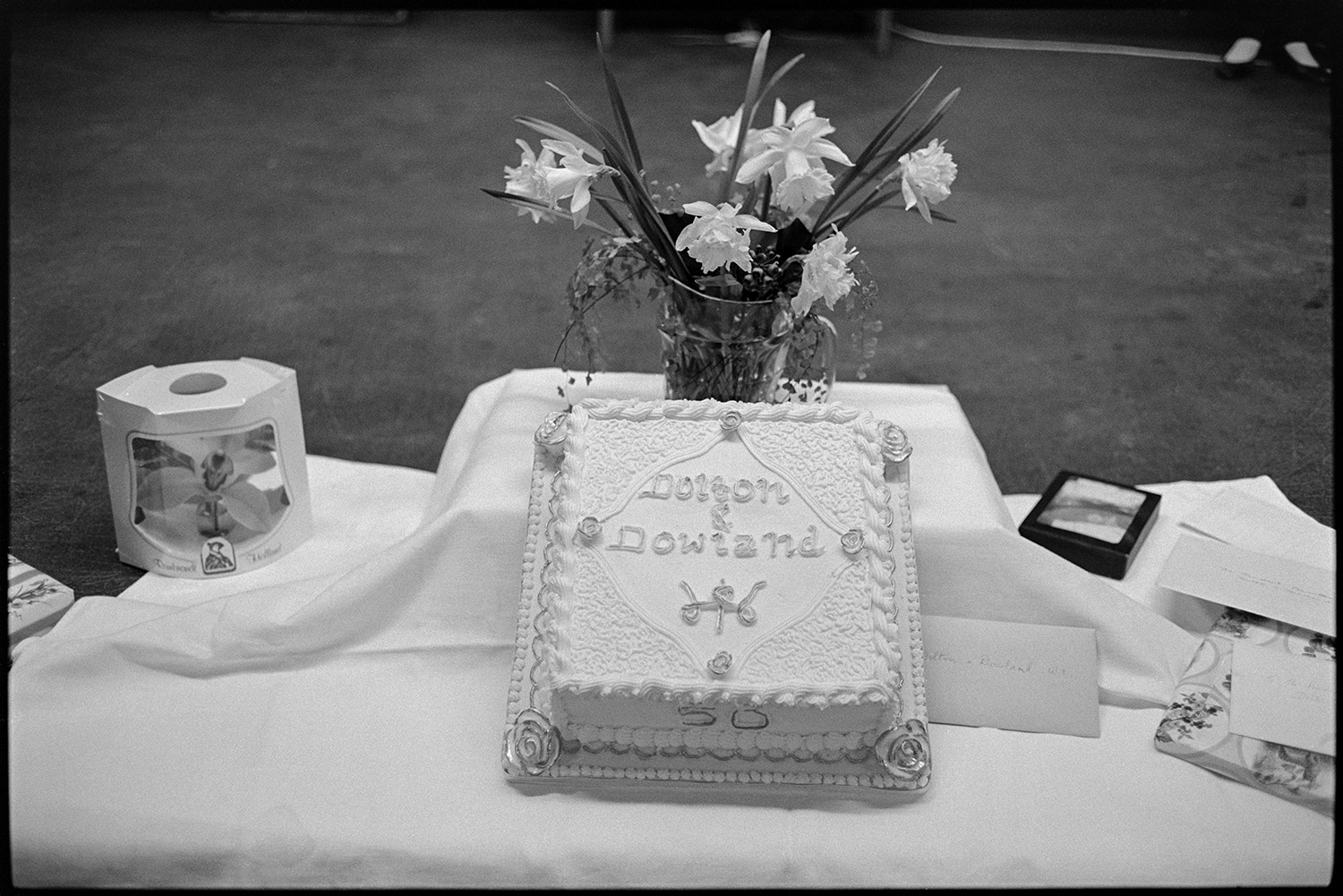 Cake for W I celebration. 
[A cake for the celebration of the fiftieth anniversary of Dolton and Dowland Women's Institute in Dolton Village Hall. A vase of flowers is behind the cake.]